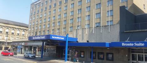 Un hotel con un toldo de entrada azul, un letrero que dice 'Bronte Suite' y un edificio grande al fondo.