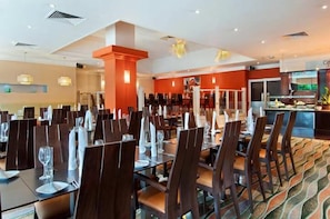 Un restaurante con varias mesas y sillas, una barra con vitrina y una alfombra estampada.