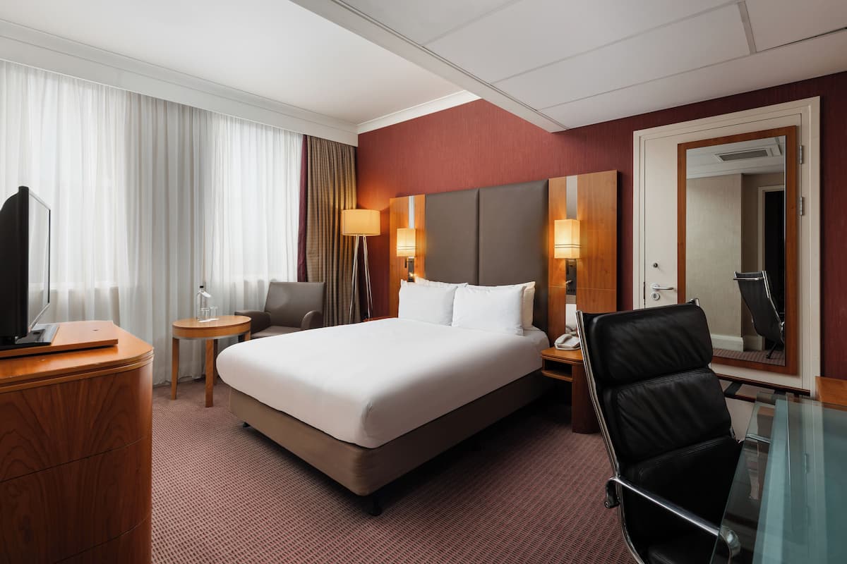 A hotel room with a large bed, a desk, a chair, a TV, and a mirror.