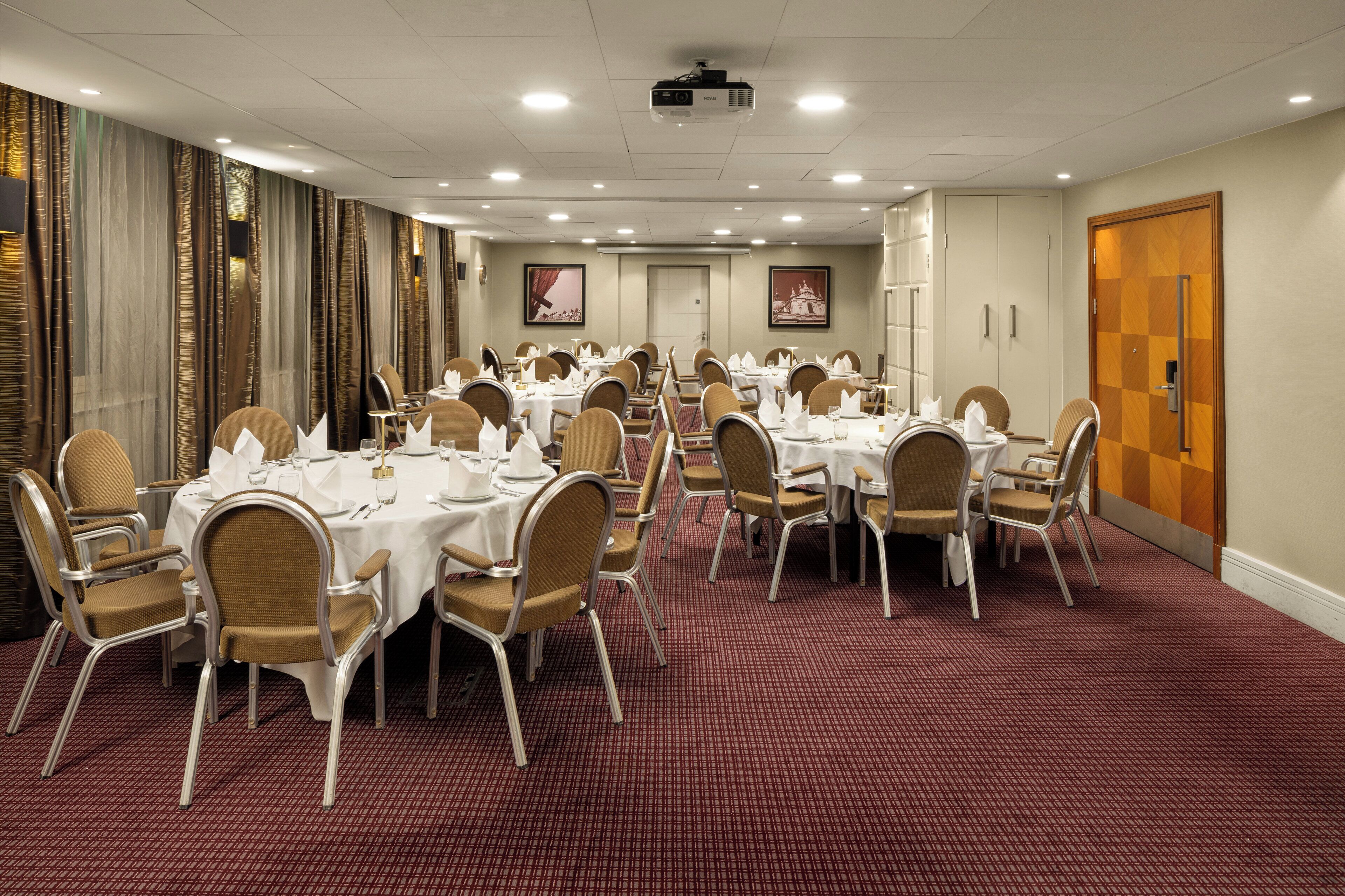 A conference room with multiple tables set for dining, equipped with chairs and tables, and a carpeted floor.