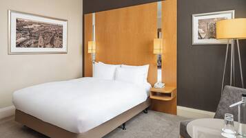 Habitación de hotel con una cama grande, una mesita de noche con lámpara, una silla y dos cuadros en la pared.