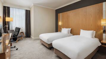 A hotel room with two beds, a desk, a chair, and a lamp.