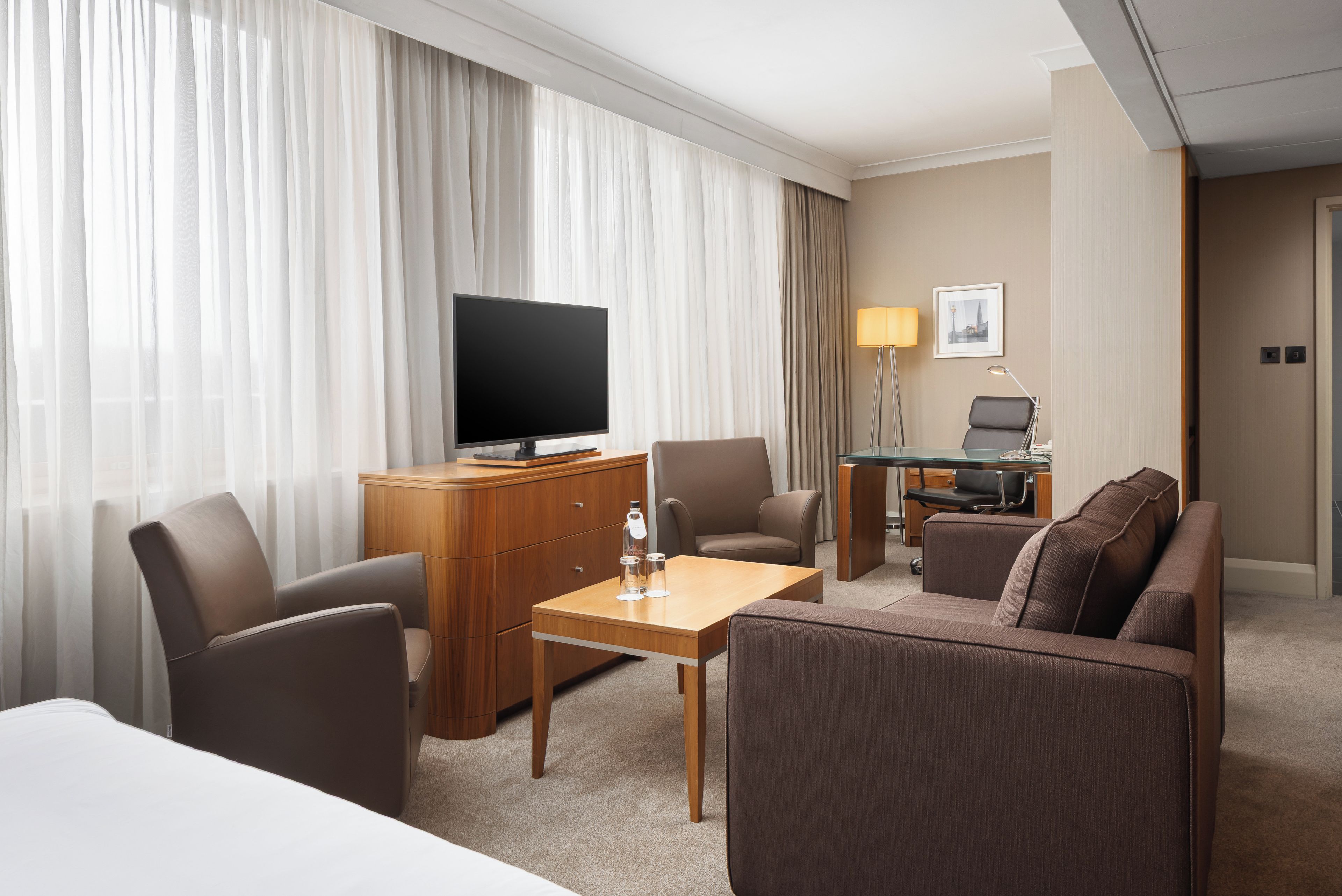Une chambre d’hôtel équipée d’un lit, d’une télévision, d’un bureau, d’une chaise, d’un canapé et d’une lampe.
