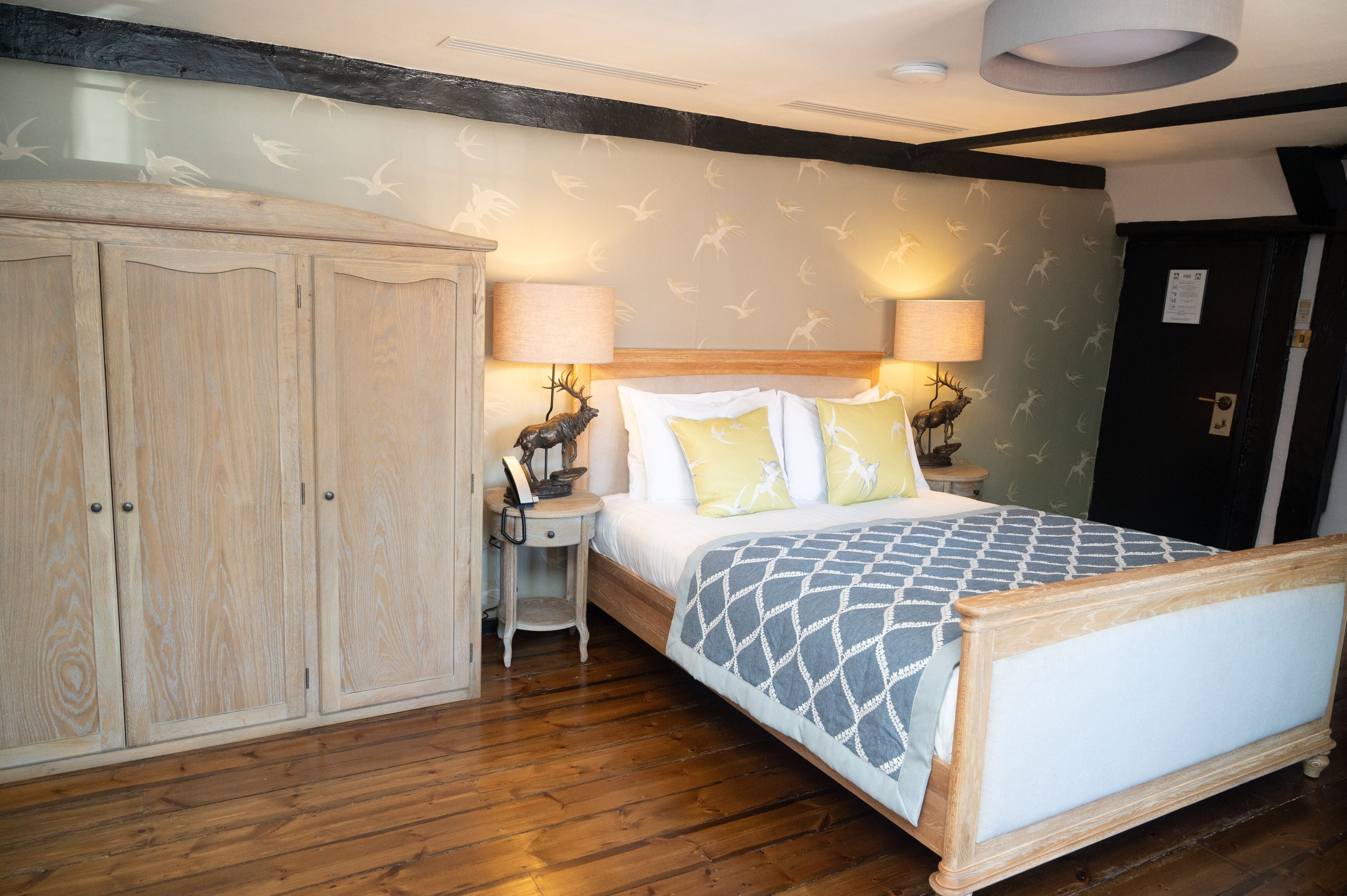 Un dormitorio con cama de madera, dos mesitas de noche con lámparas, un armario y una pared con un diseño de pájaros.