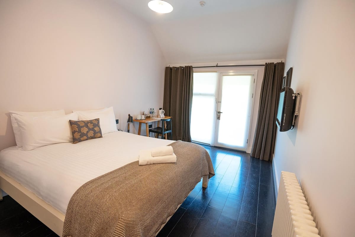 A hotel room with a large bed, a desk, and a view of the outdoors through a sliding door.