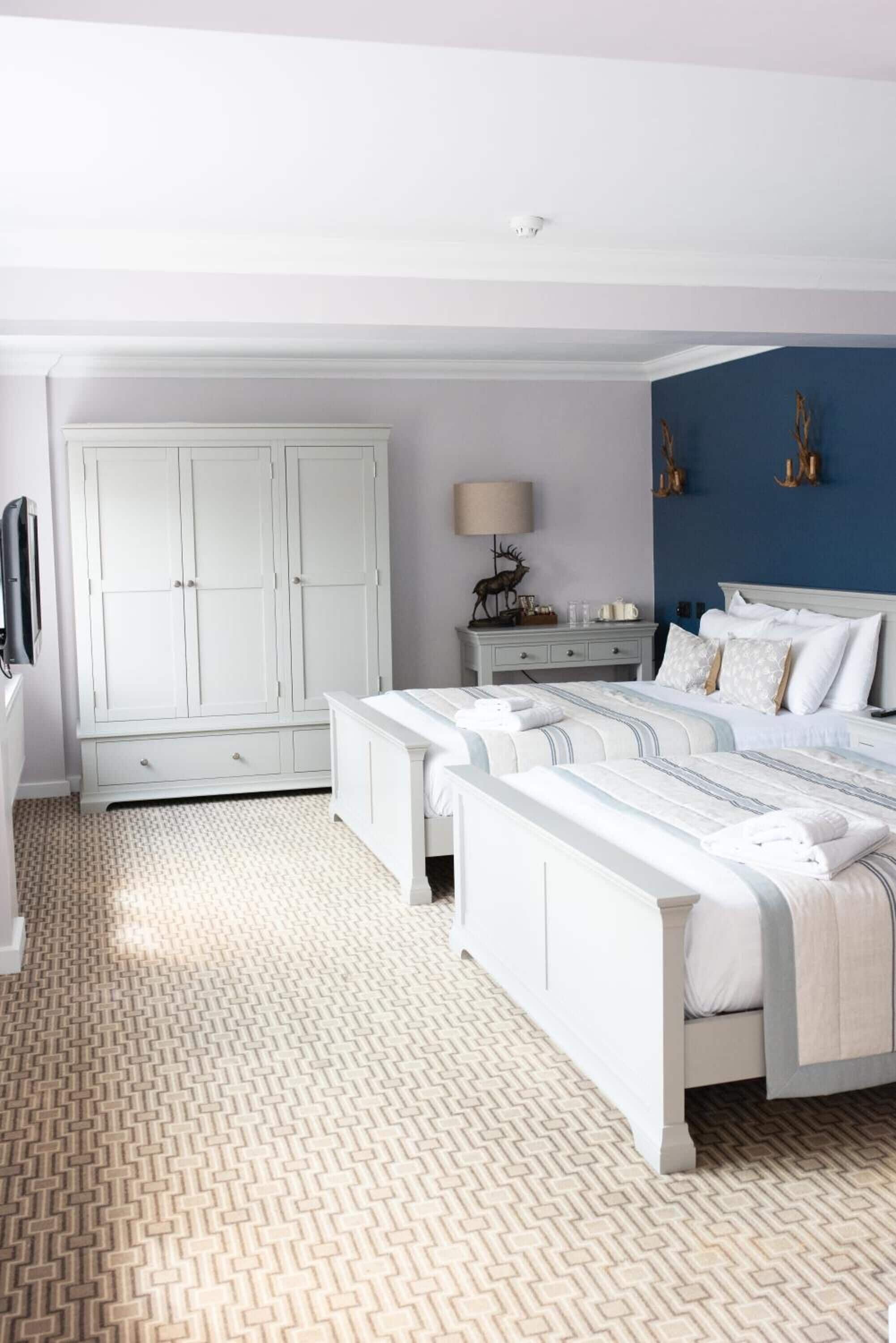 Quarto com duas camas, guarda-roupa, mesa de cabeceira e abajur.