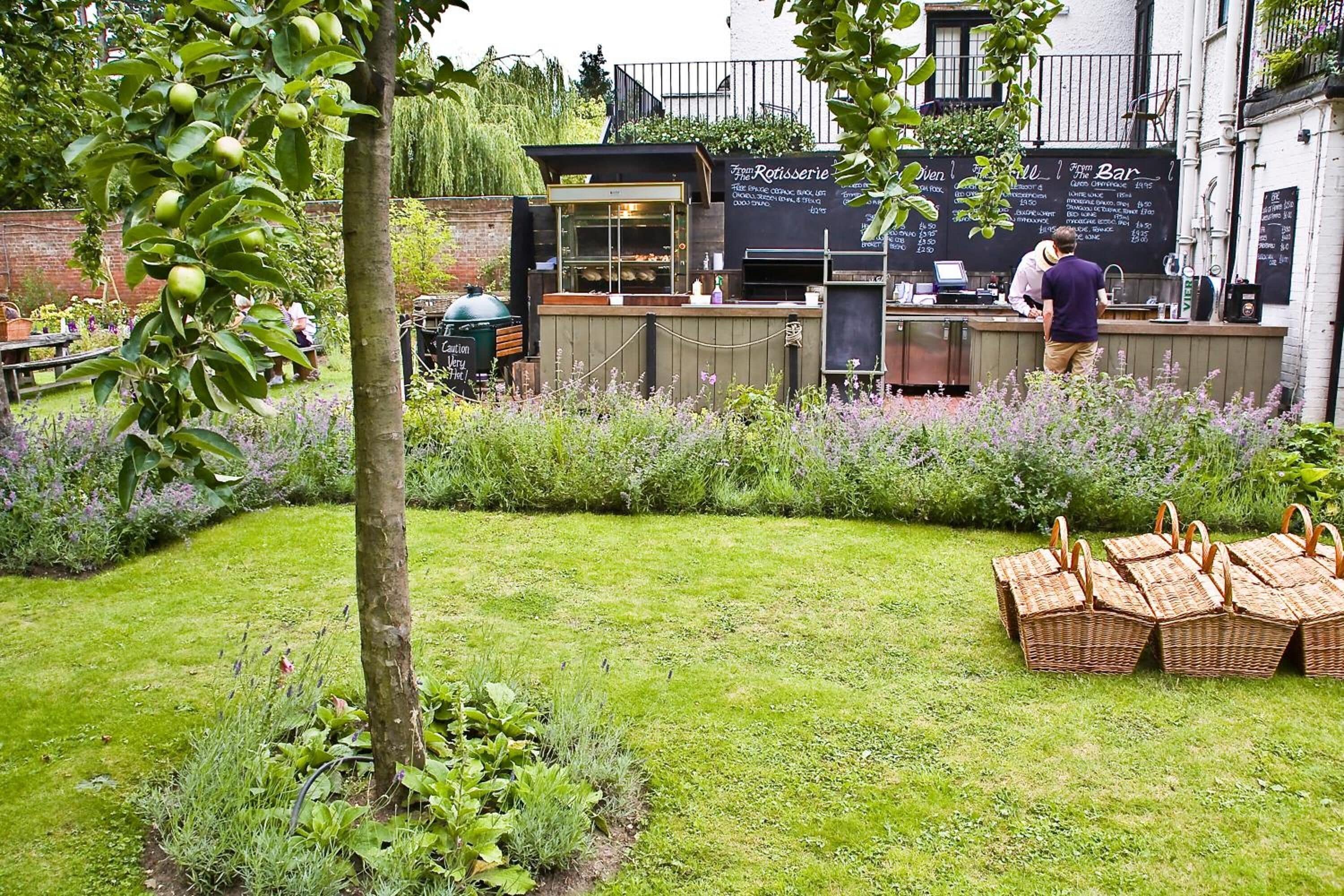 Un caffè con posti a sedere all'aperto, una lavagna con il menù e un'area giardino con cesti da picnic.