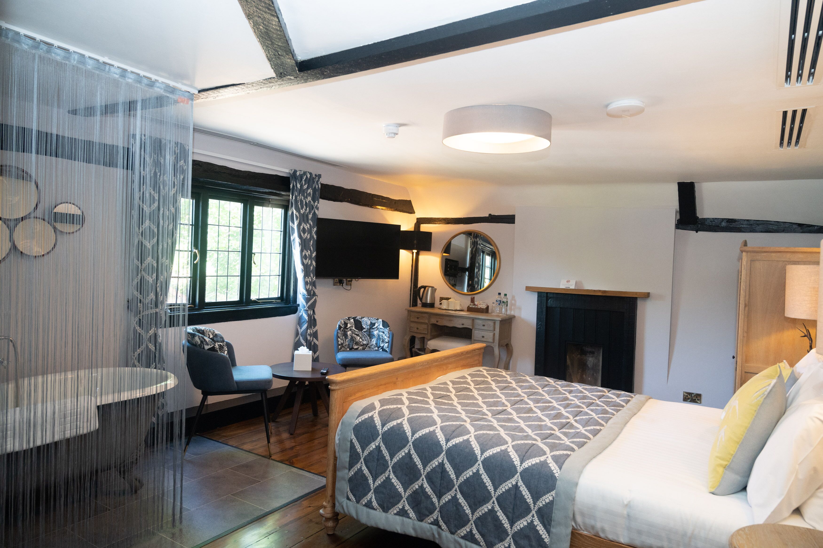 A bedroom with a bed, a desk, a chair, a mirror, and a fireplace.