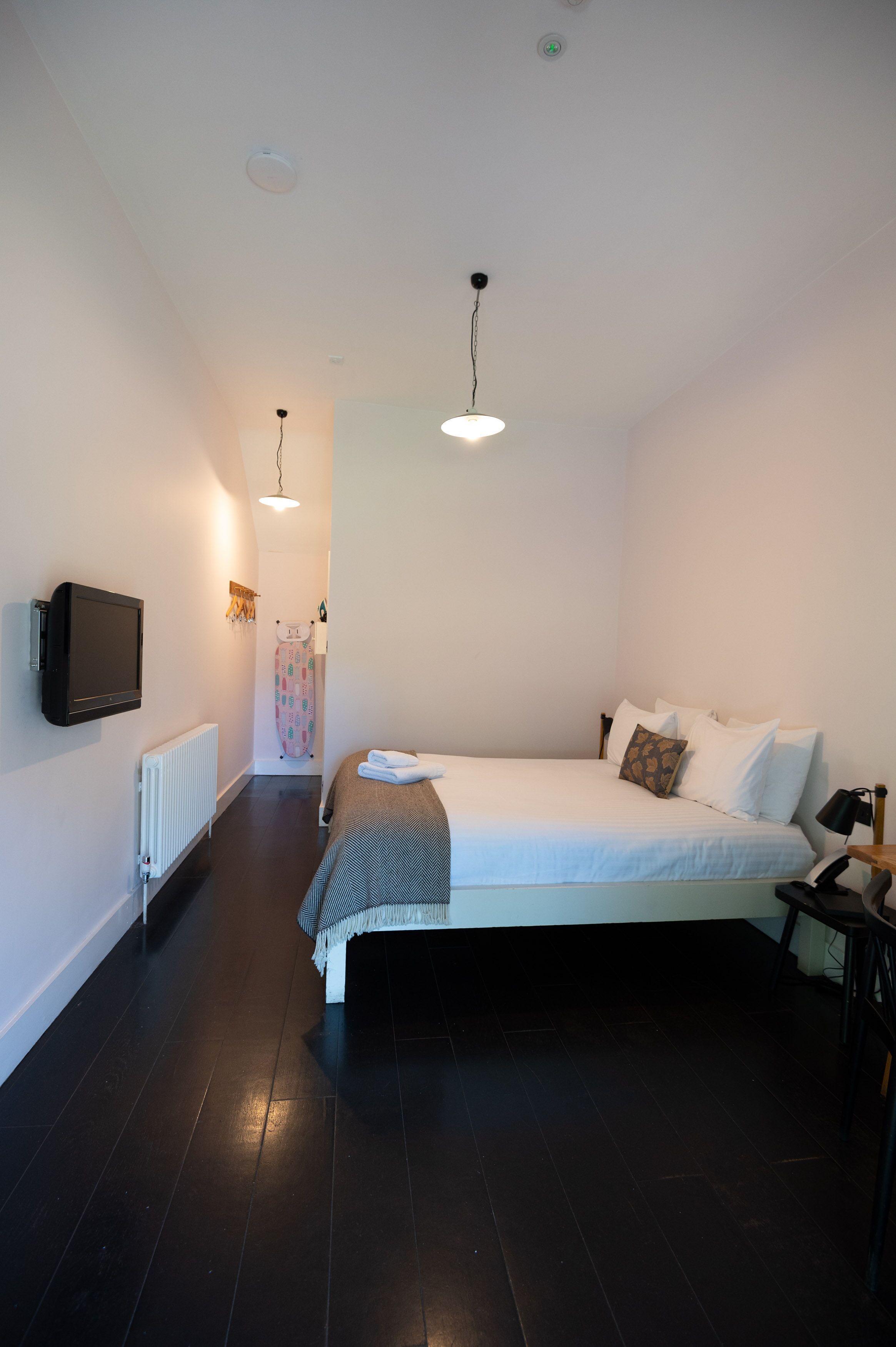 Un dormitorio con cama, mesita de noche, lámpara y televisor en la pared.