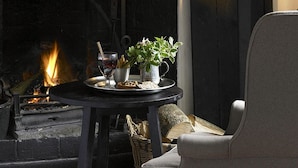 Un rincón acogedor con una chimenea, una mesa con bebidas y aperitivos, y un sillón cómodo.