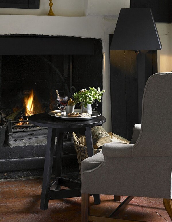 Un rincón acogedor con una chimenea, una mesa con bebidas y aperitivos, y un sillón cómodo.