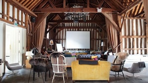 Interior rústico de estilo granero con una gran pantalla blanca, vigas de madera y una mezcla de muebles modernos y clásicos.