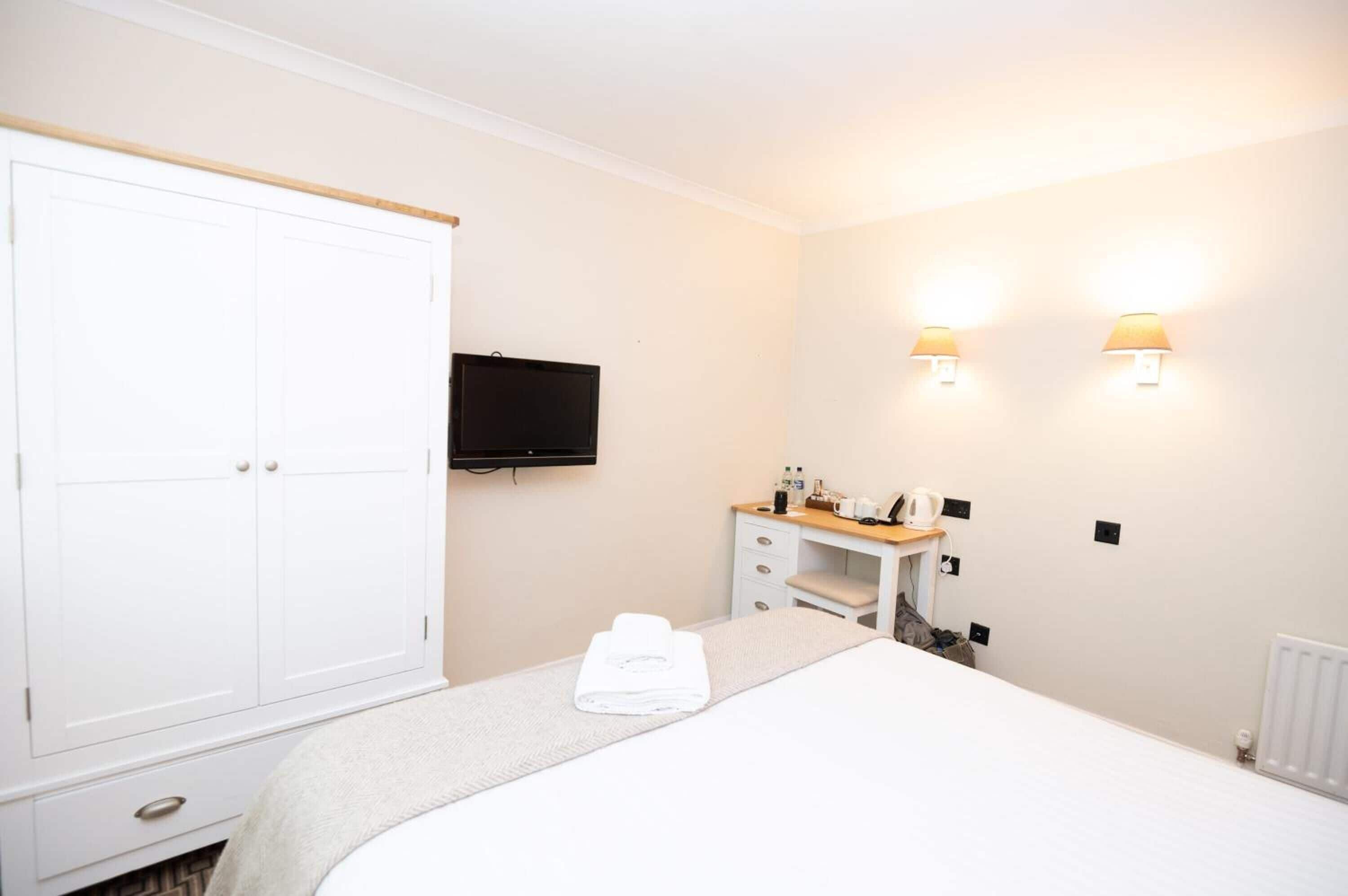 A hotel room with a bed, a wardrobe, a desk with a lamp, and a television.
