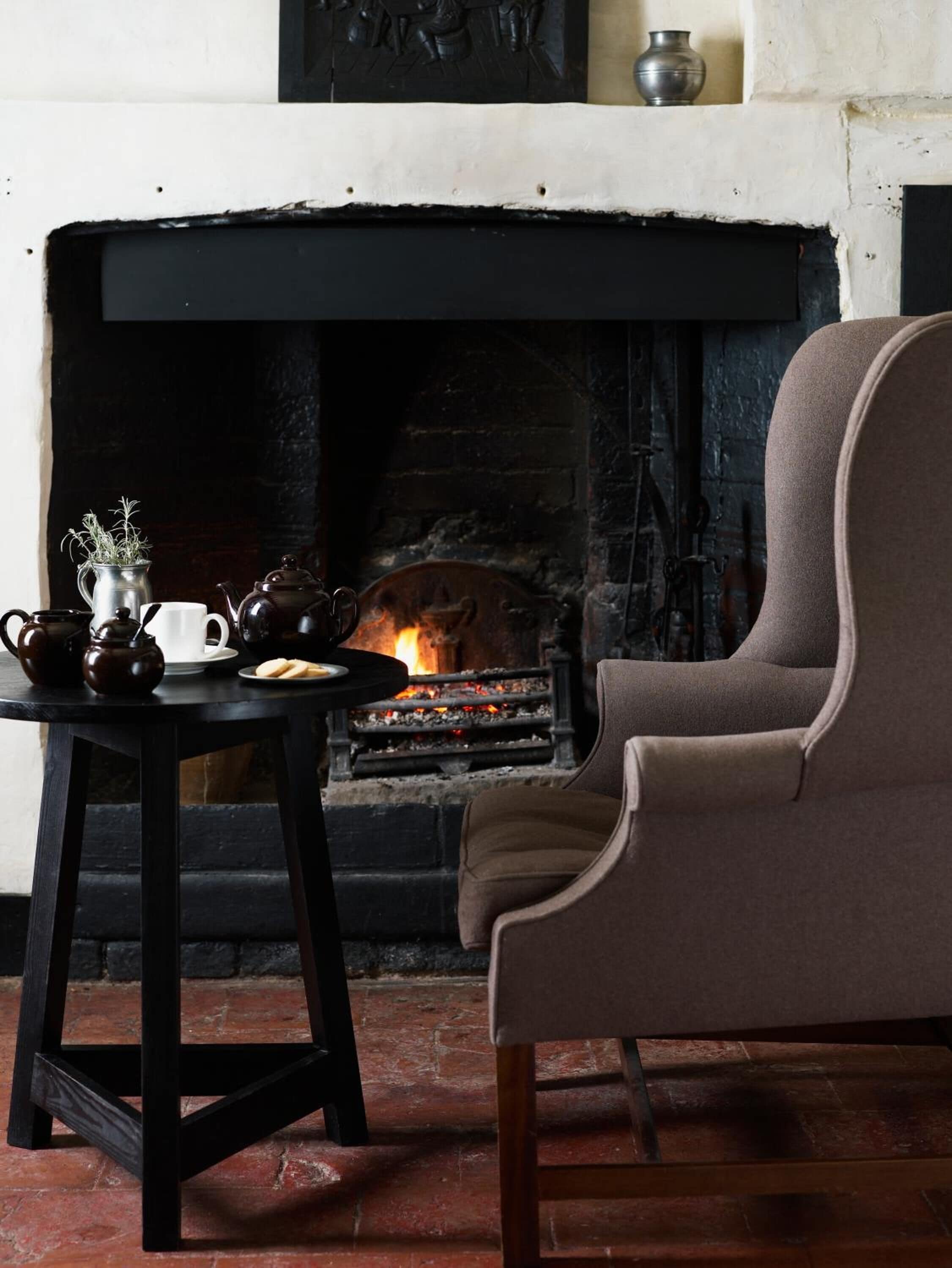 Une pièce chaleureuse avec une cheminée, une table où est disposé un service à thé et un fauteuil confortable.