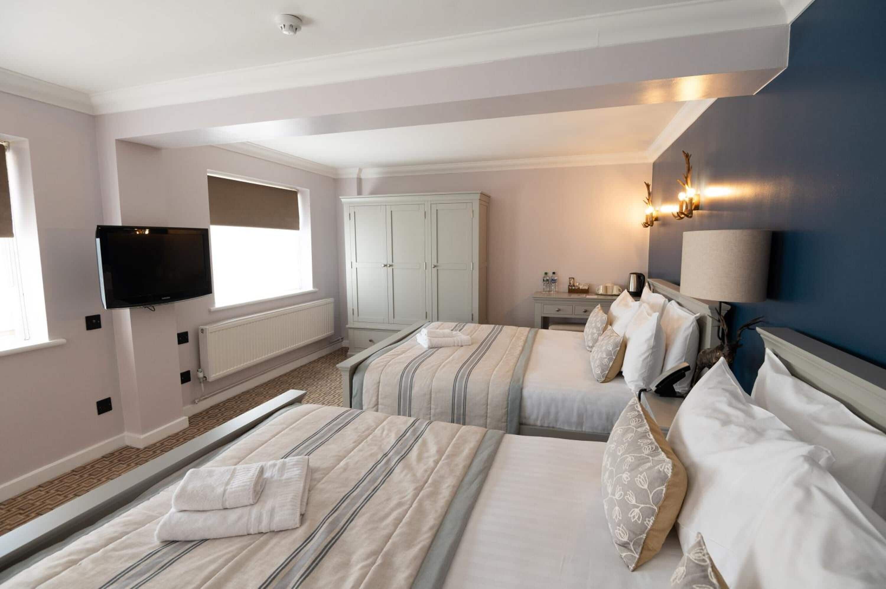 Ein Hotelzimmer mit zwei Betten, einem Fernseher, einem Schrank, einem Schreibtisch mit Lampe und Blick ins Freie.