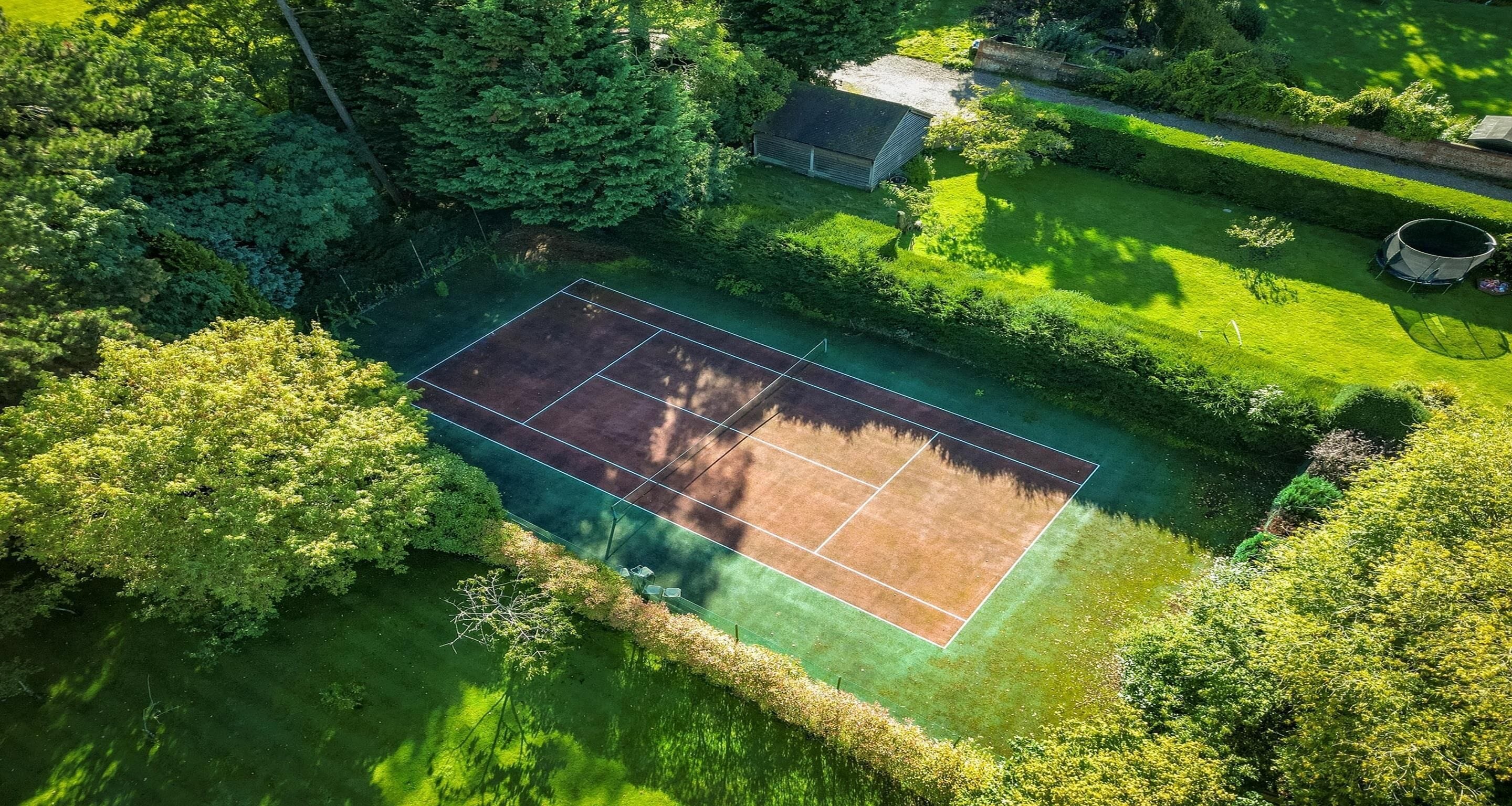 An aerial view of a tennis court surrounded by lush greenery and a small building.