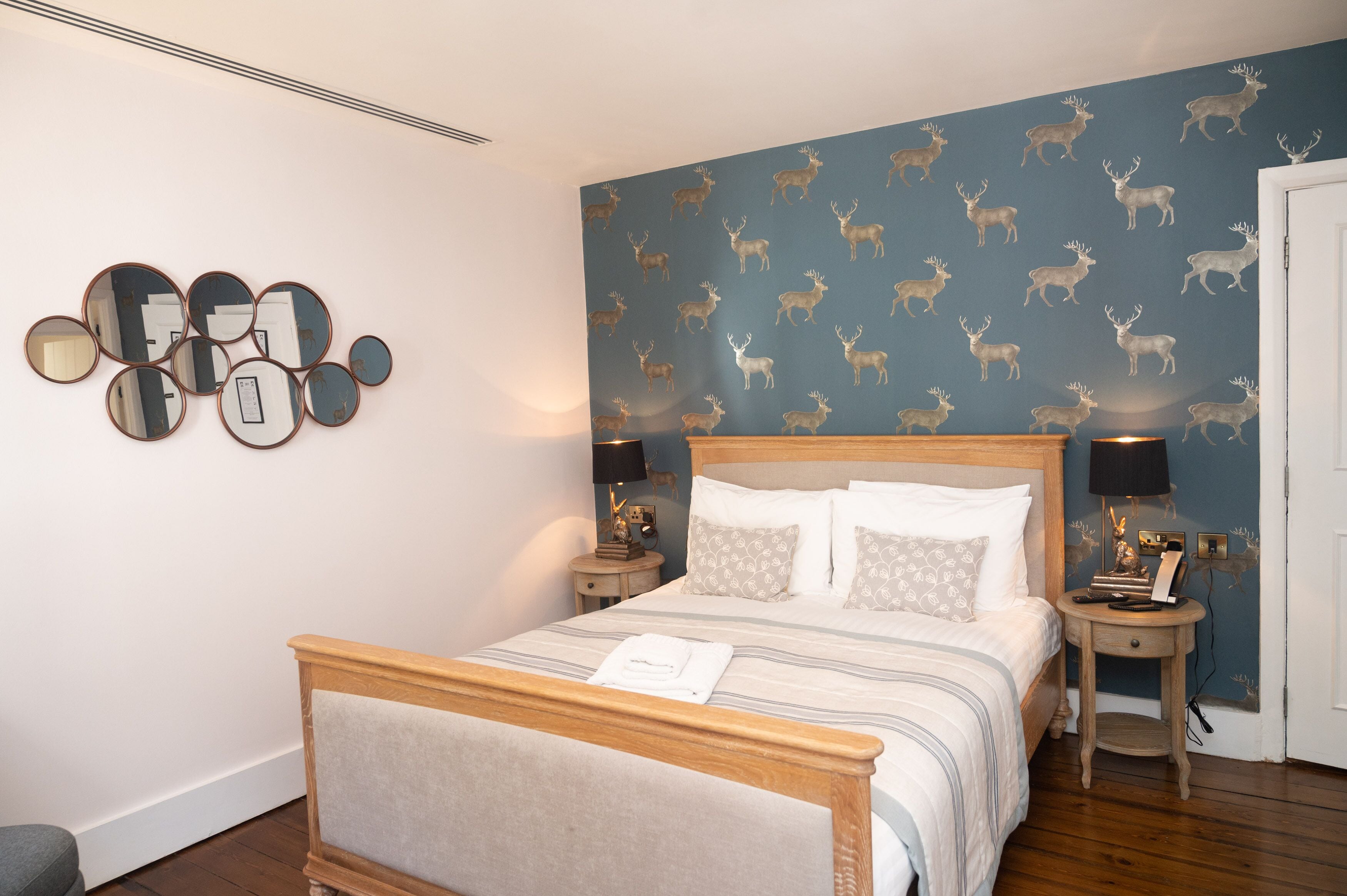 A neatly arranged bedroom with a bed, bedside tables, and a wall with a deer pattern.