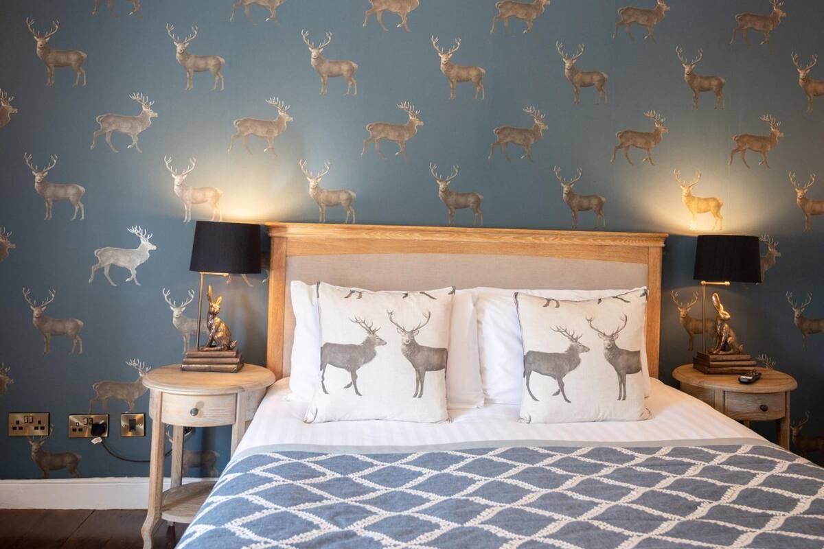 A bedroom with a patterned wallpaper of deer, a wooden headboard, and two bedside tables with lamps.
