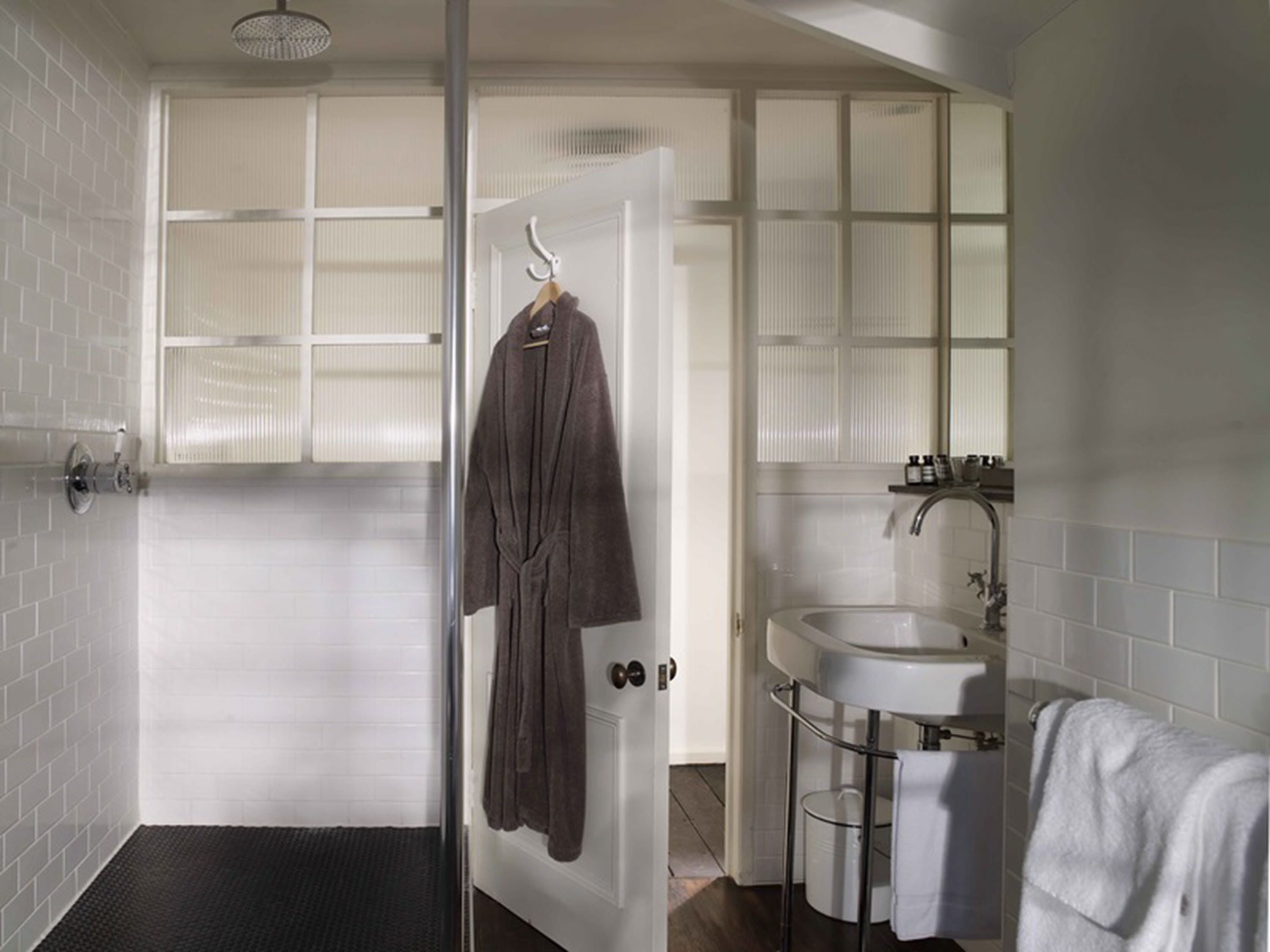 Un baño con mampara de vidrio, un lavabo blanco y un perchero para toallas.