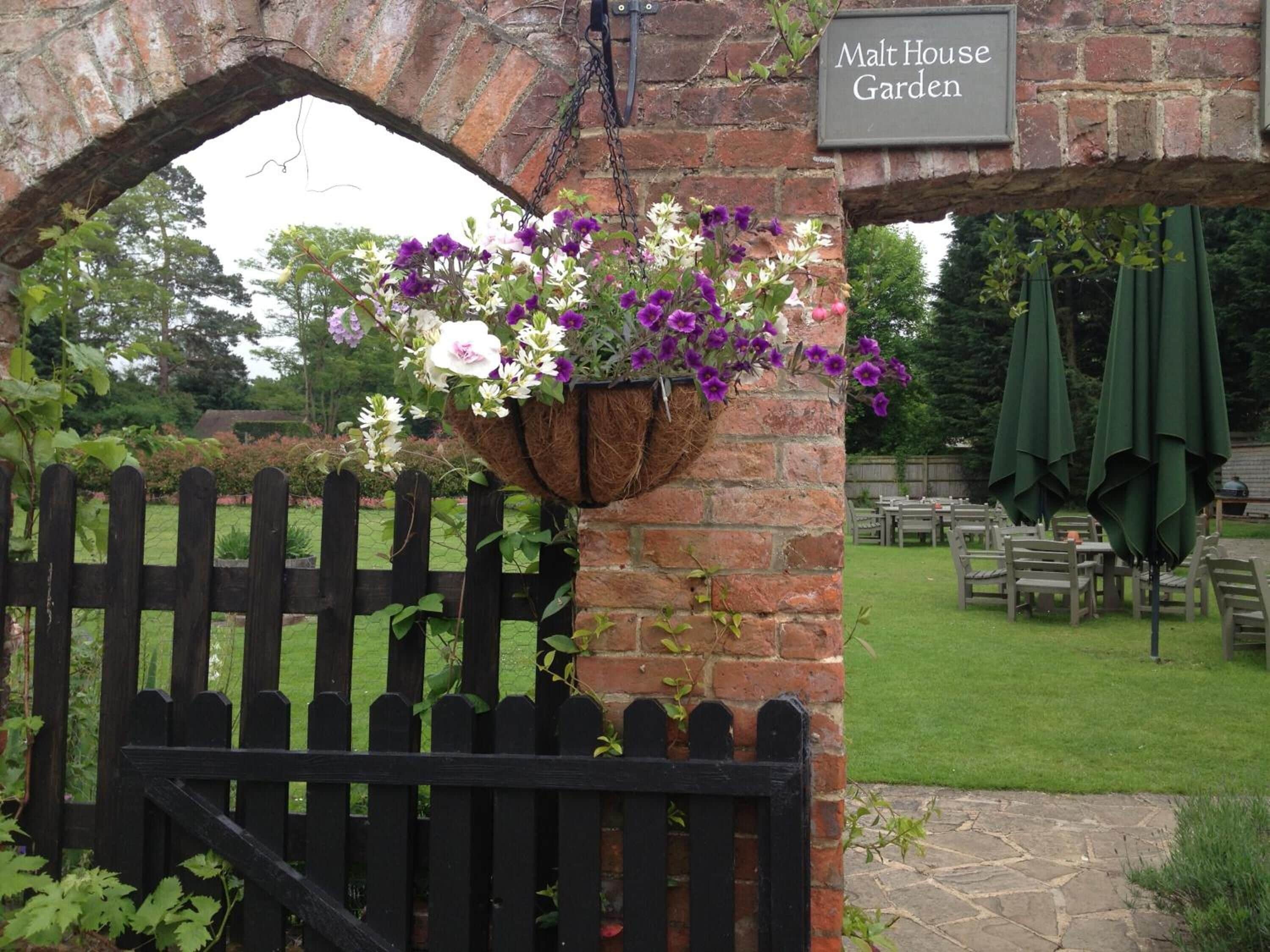A brick archway with a hanging flower basket and a sign reading "Malt House Garden".