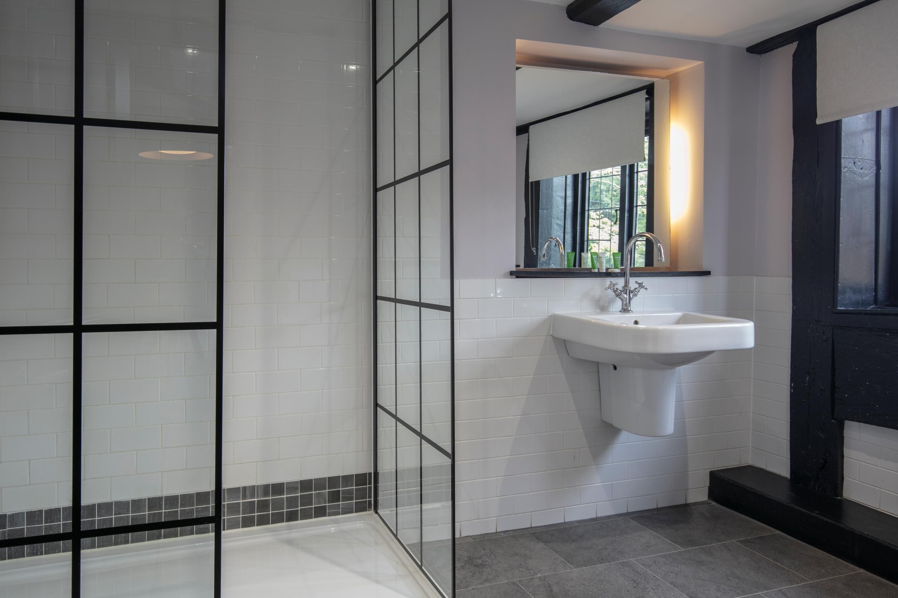 Un baño moderno con cabina de ducha de vidrio, un lavamanos blanco y un espejo encima.