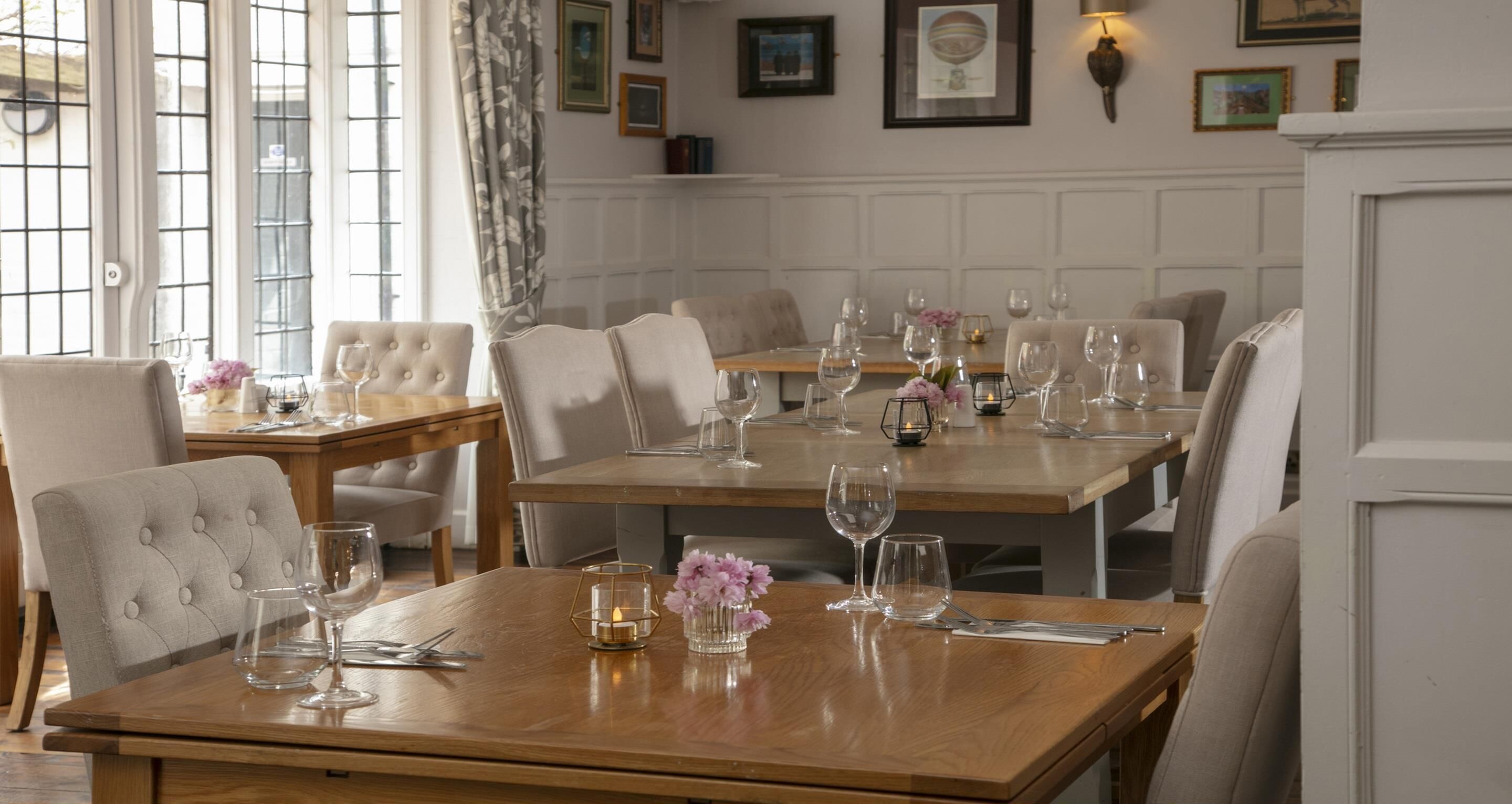 A dining area with wooden tables, white upholstered chairs, and glassware.