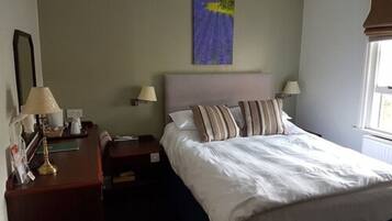 A hotel room with a bed, two bedside tables, lamps, a nightstand, a mirror, and a window with curtains.