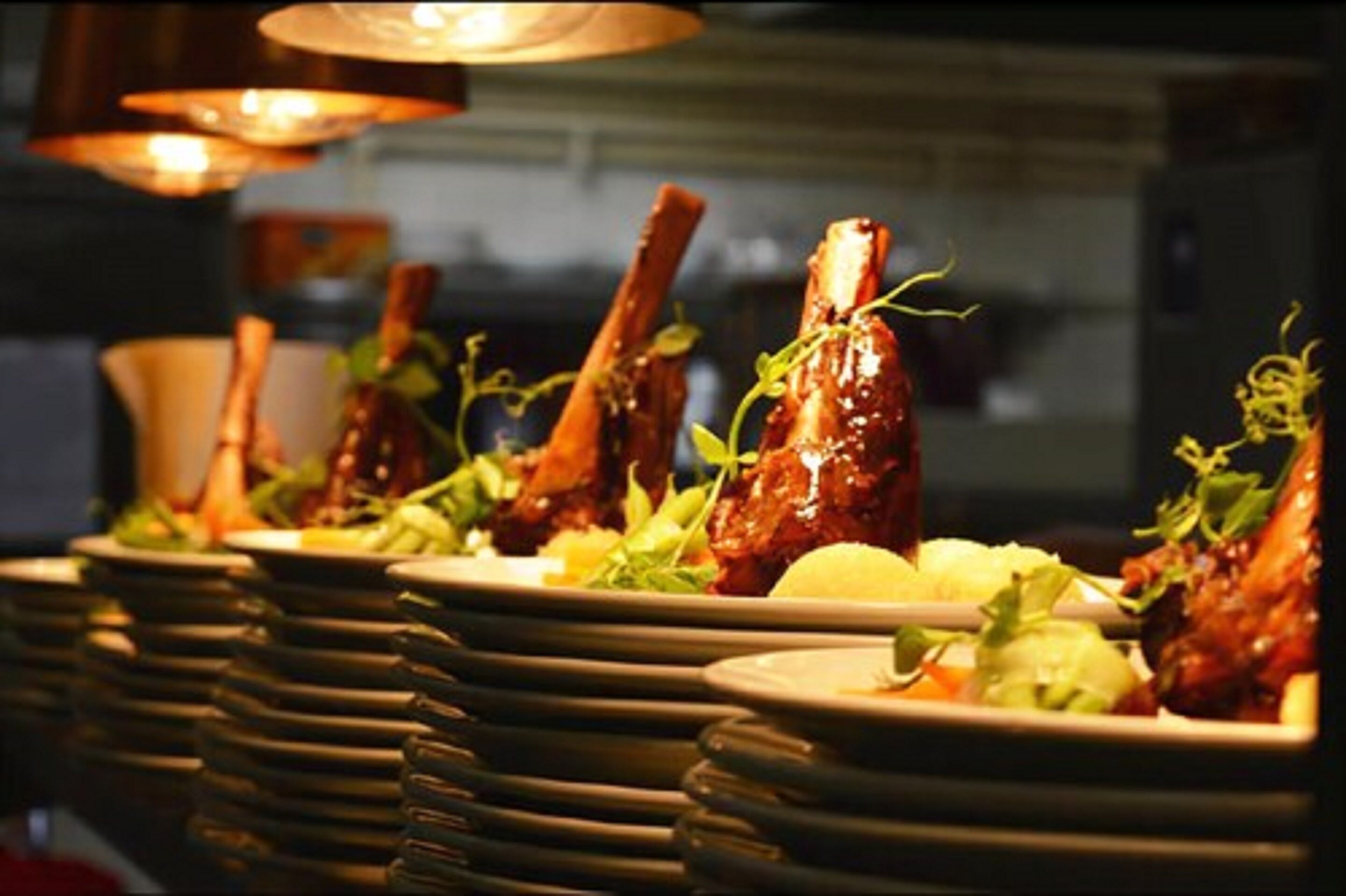 A row of plates with roasted lamb shanks and greens.