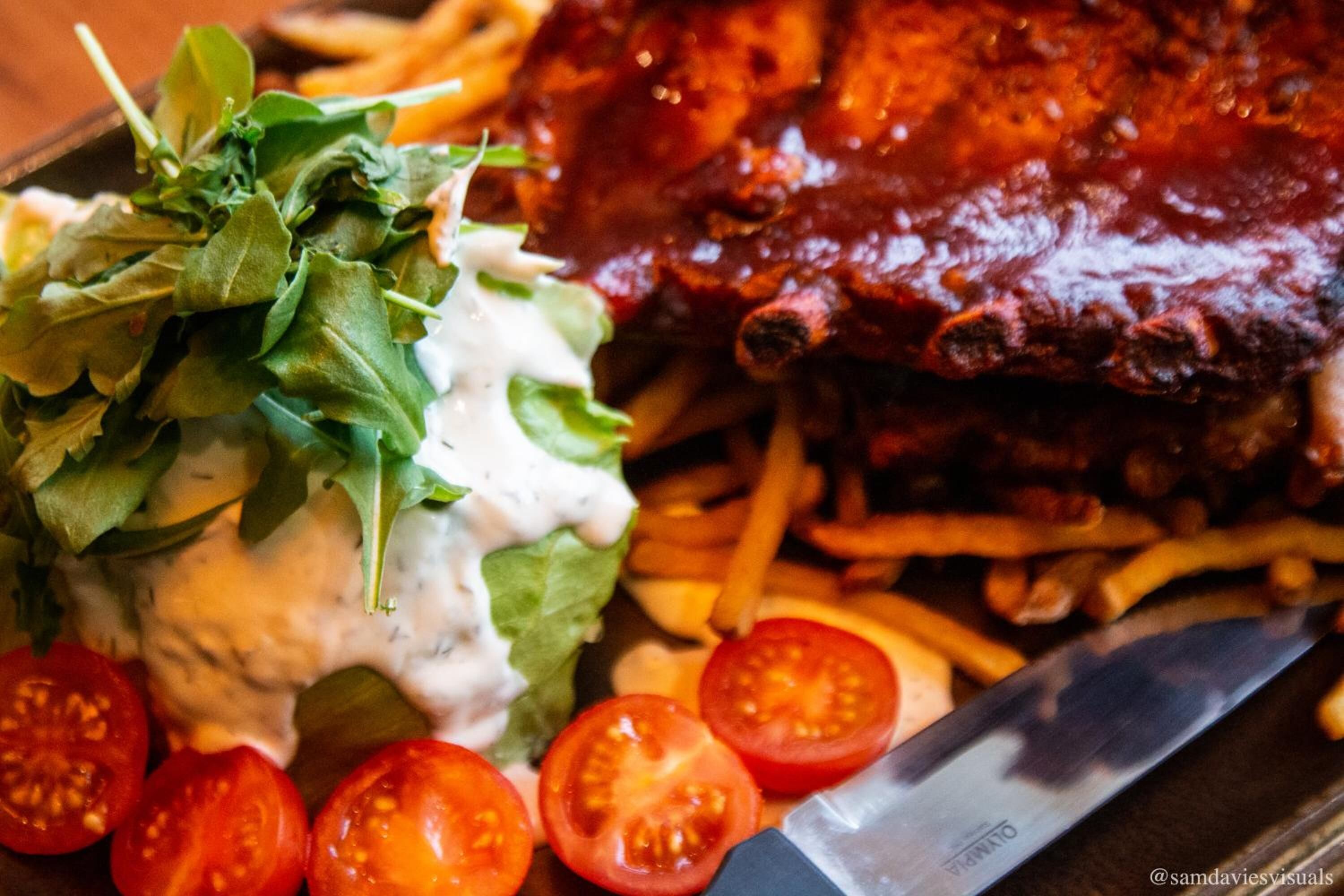 A plate of food including ribs, fries, lettuce, and tomatoes.