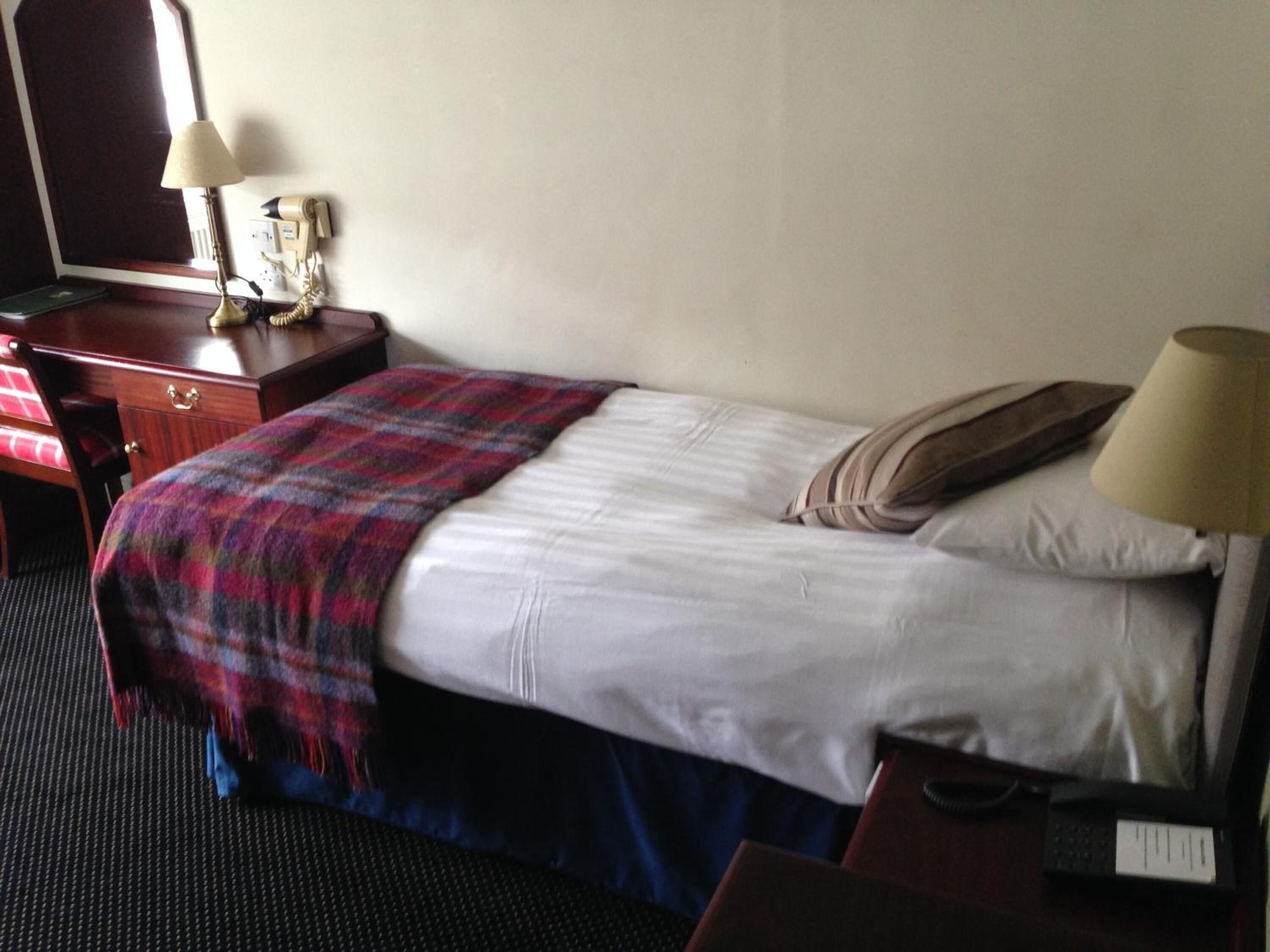 Una habitación de hotel con cama, escritorio, silla, lámpara y teléfono.
