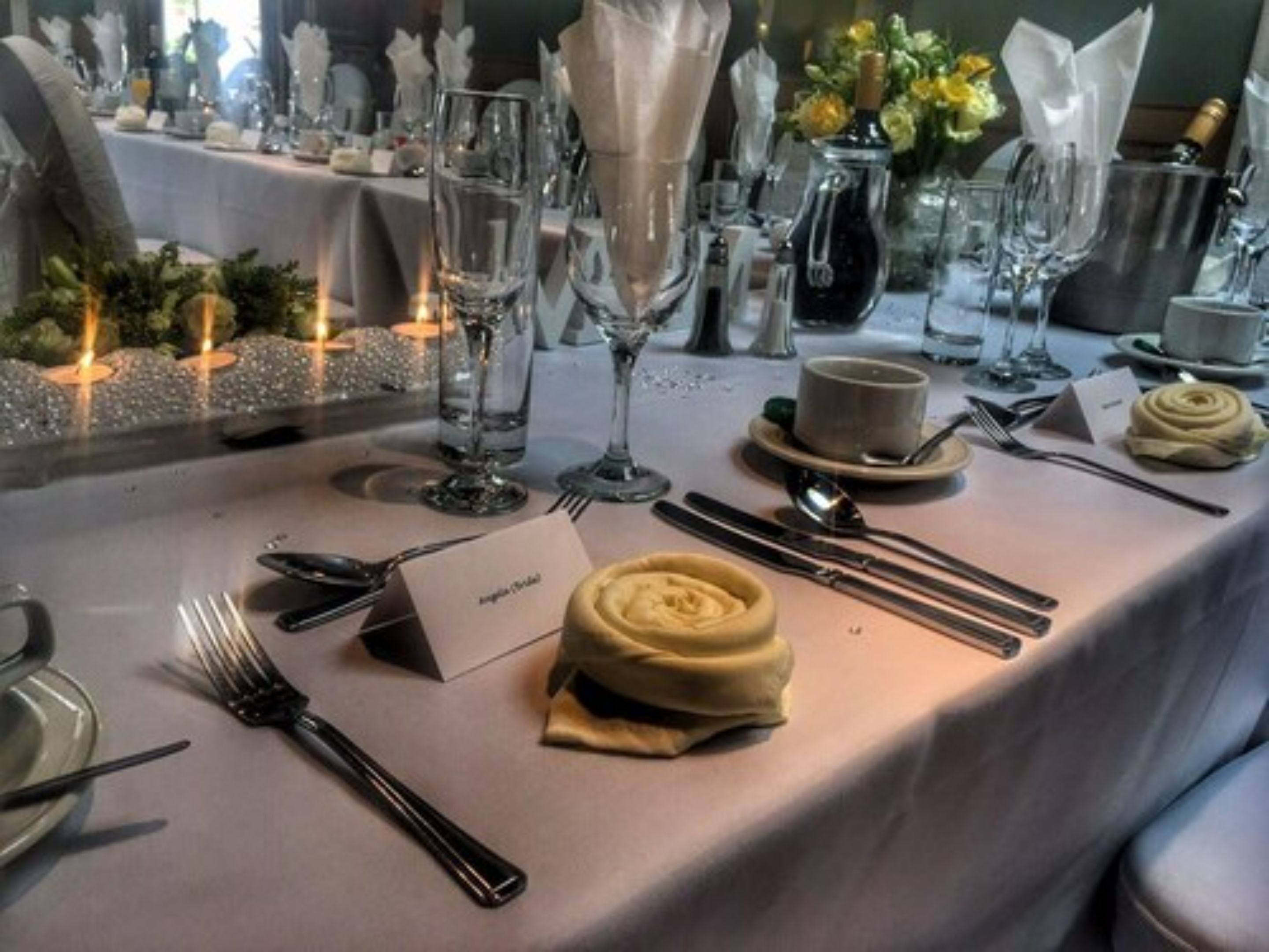 A table set for a formal dinner with a name card, cutlery, a folded napkin, and a small bowl of cream.