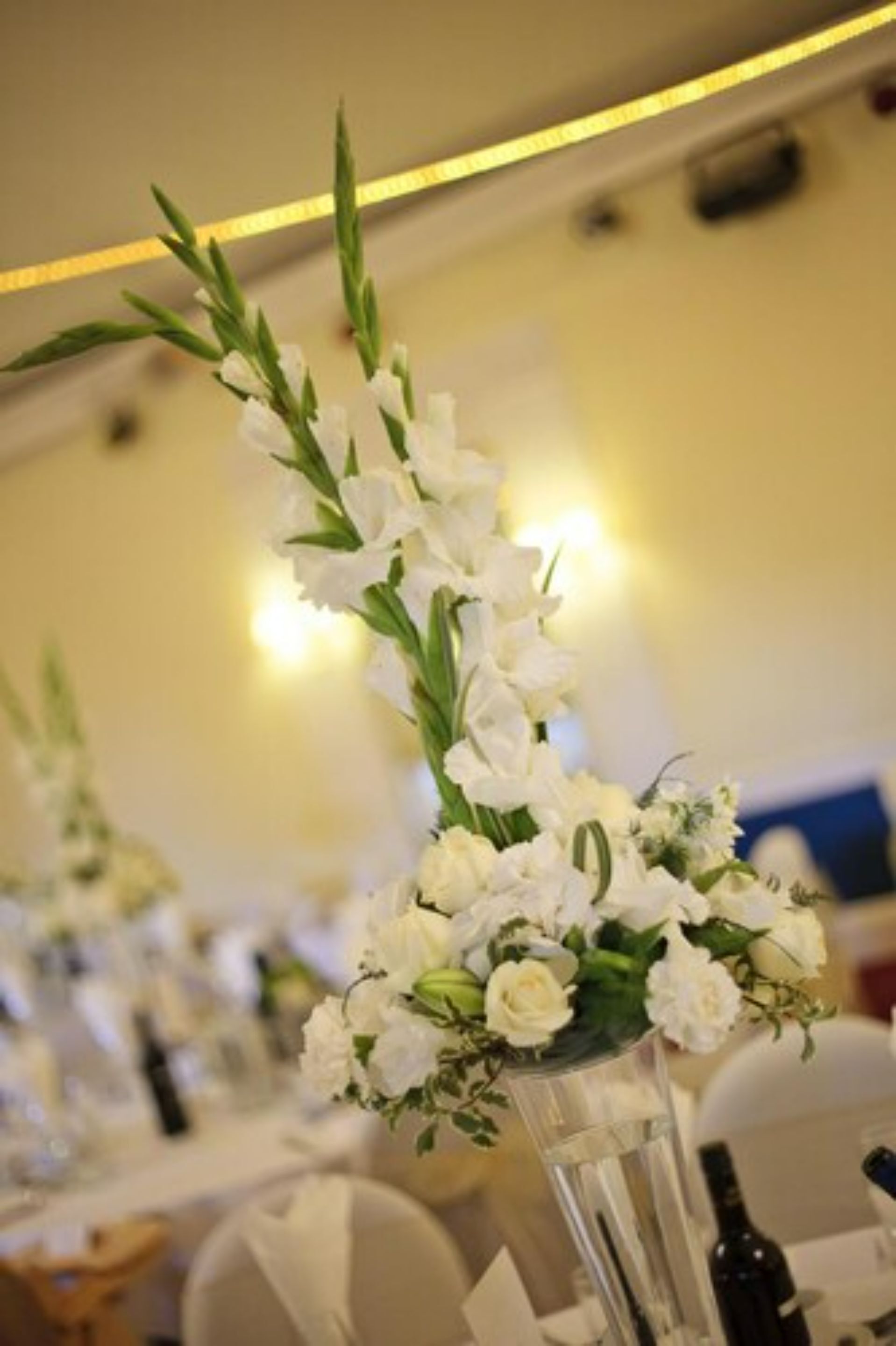 Une table sur laquelle se trouve un grand vase transparent contenant des fleurs blanches et des feuilles vertes.