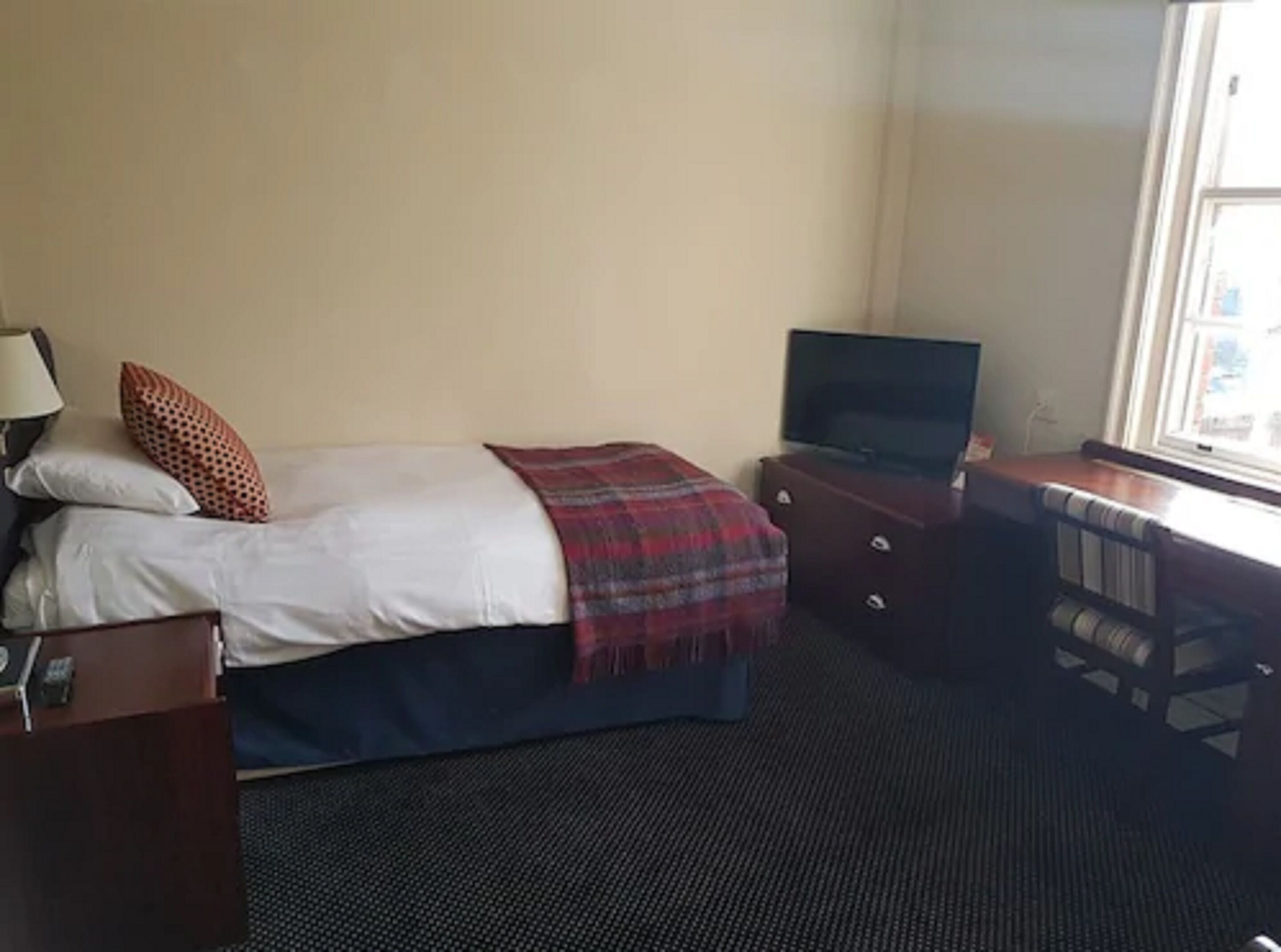Ett hotellrum med en säng, ett skrivbord med en tv, en byrå och ett fönster.