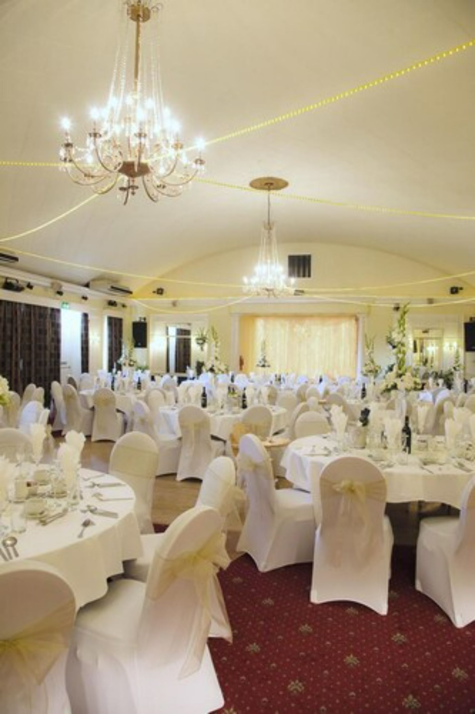 Une salle de banquet avec des tables rondes, des chaises blanches et des lustres.