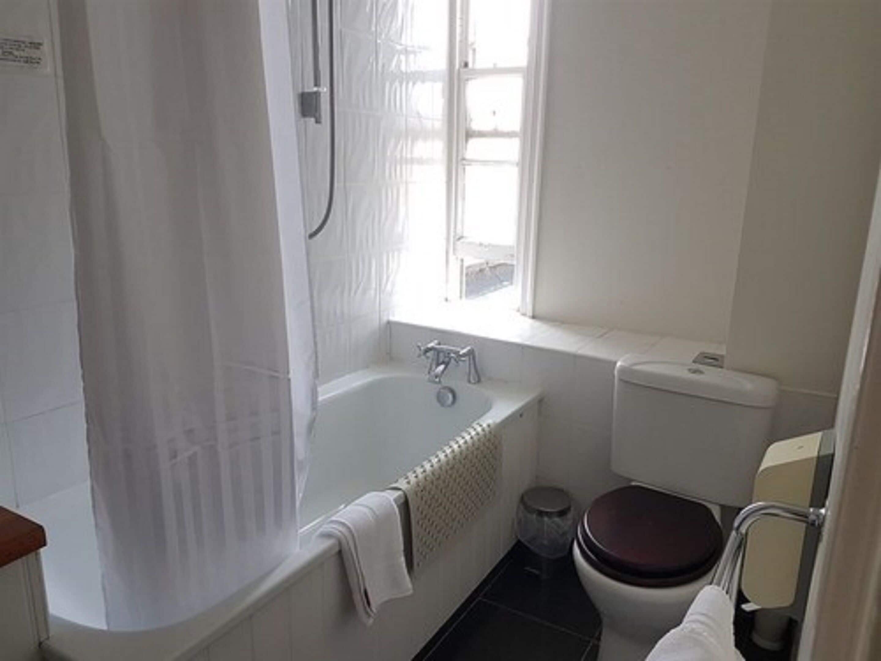 Un baño con bañera, inodoro y ventana.