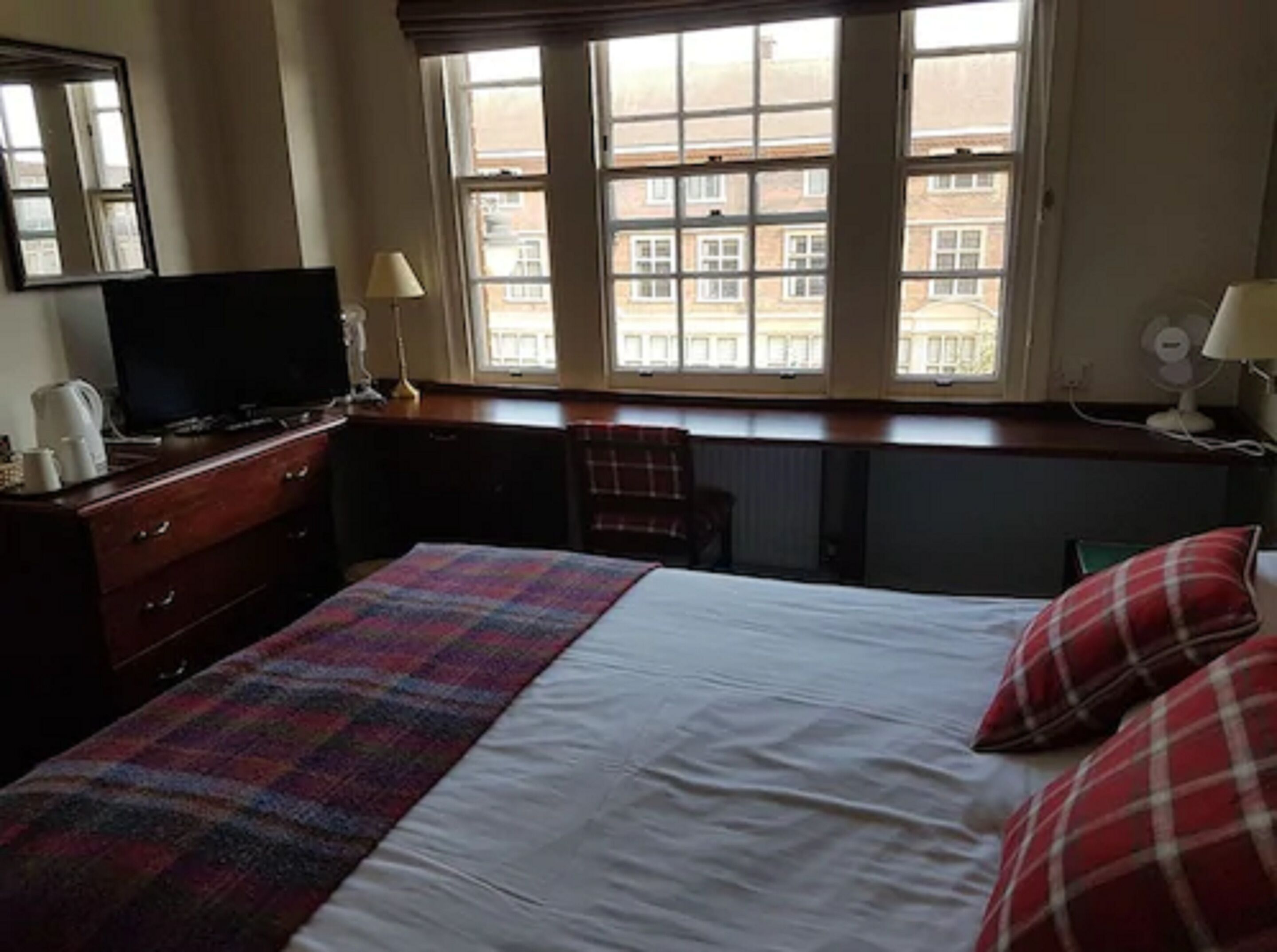 Habitación de hotel con cama, escritorio, silla, televisión y ventana con vista a edificios.