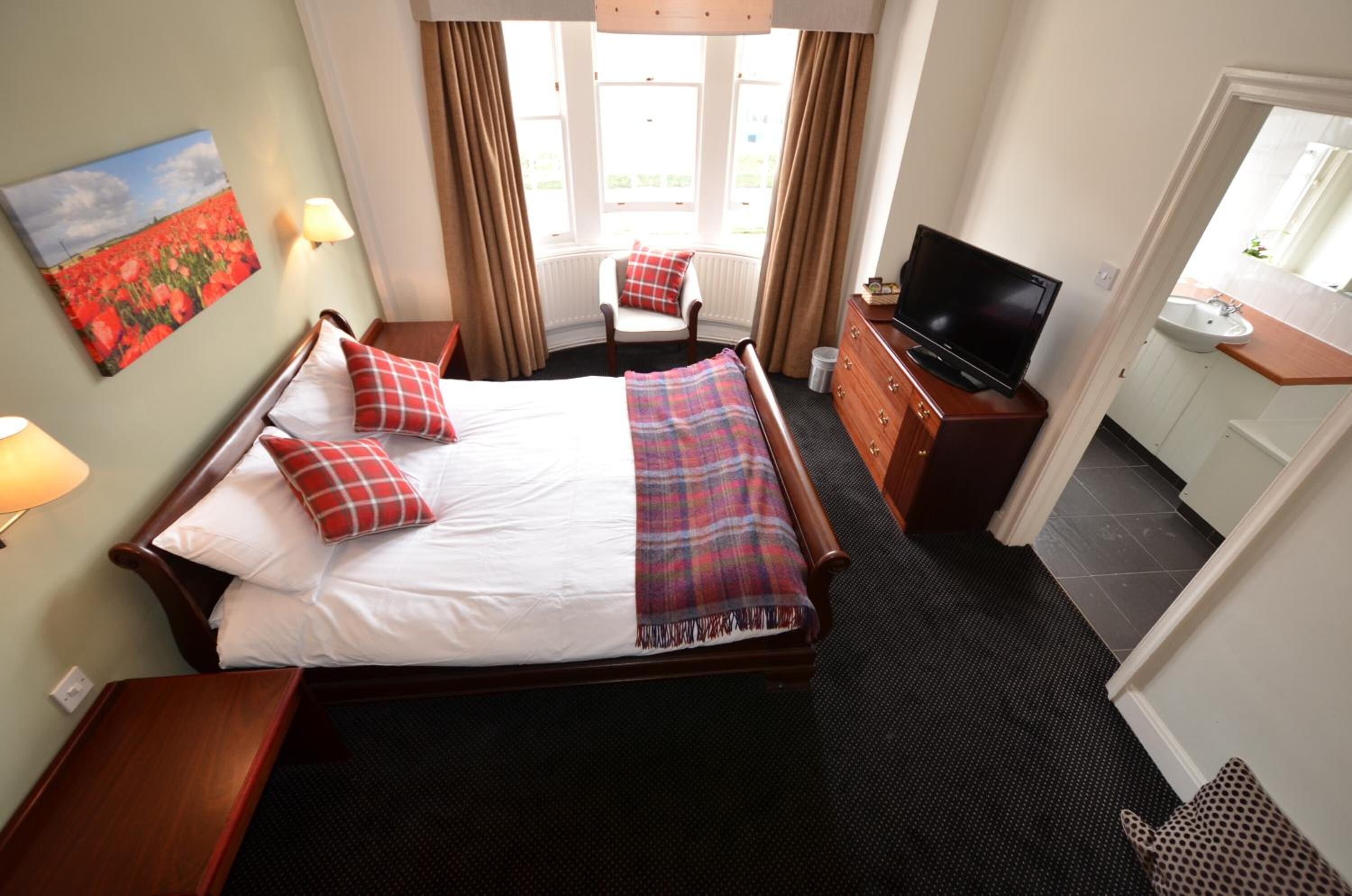 A hotel room with a large bed, a television, a desk, and a window with curtains.