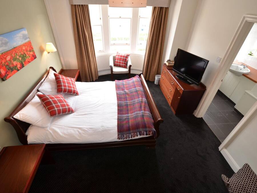 A hotel room with a large bed, a television, a desk, and a window with curtains.
