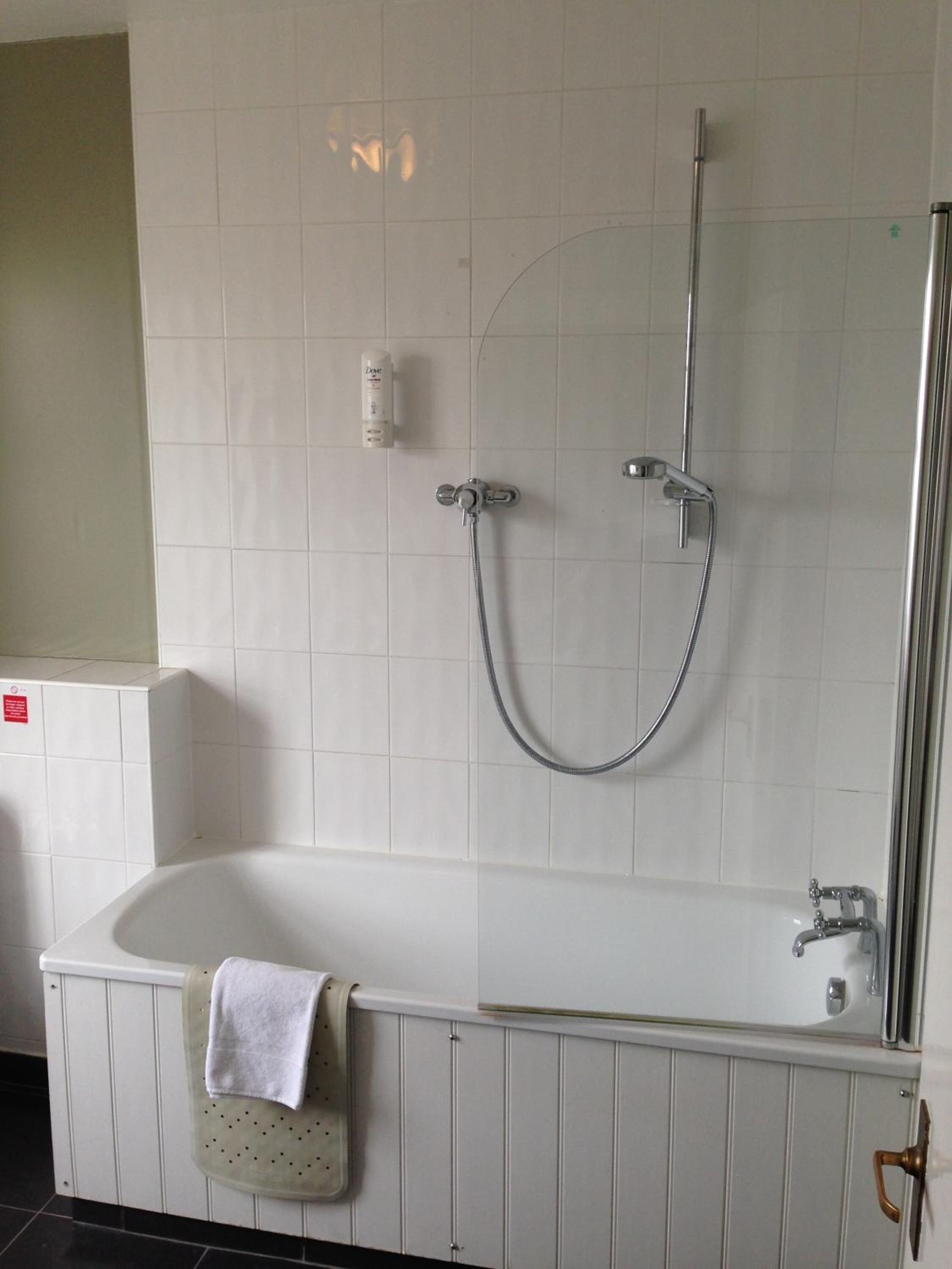 Une salle de bain avec une baignoire blanche, une douche équipée d’un pommeau de douche à main et un porte-serviettes sur lequel est posée une serviette.