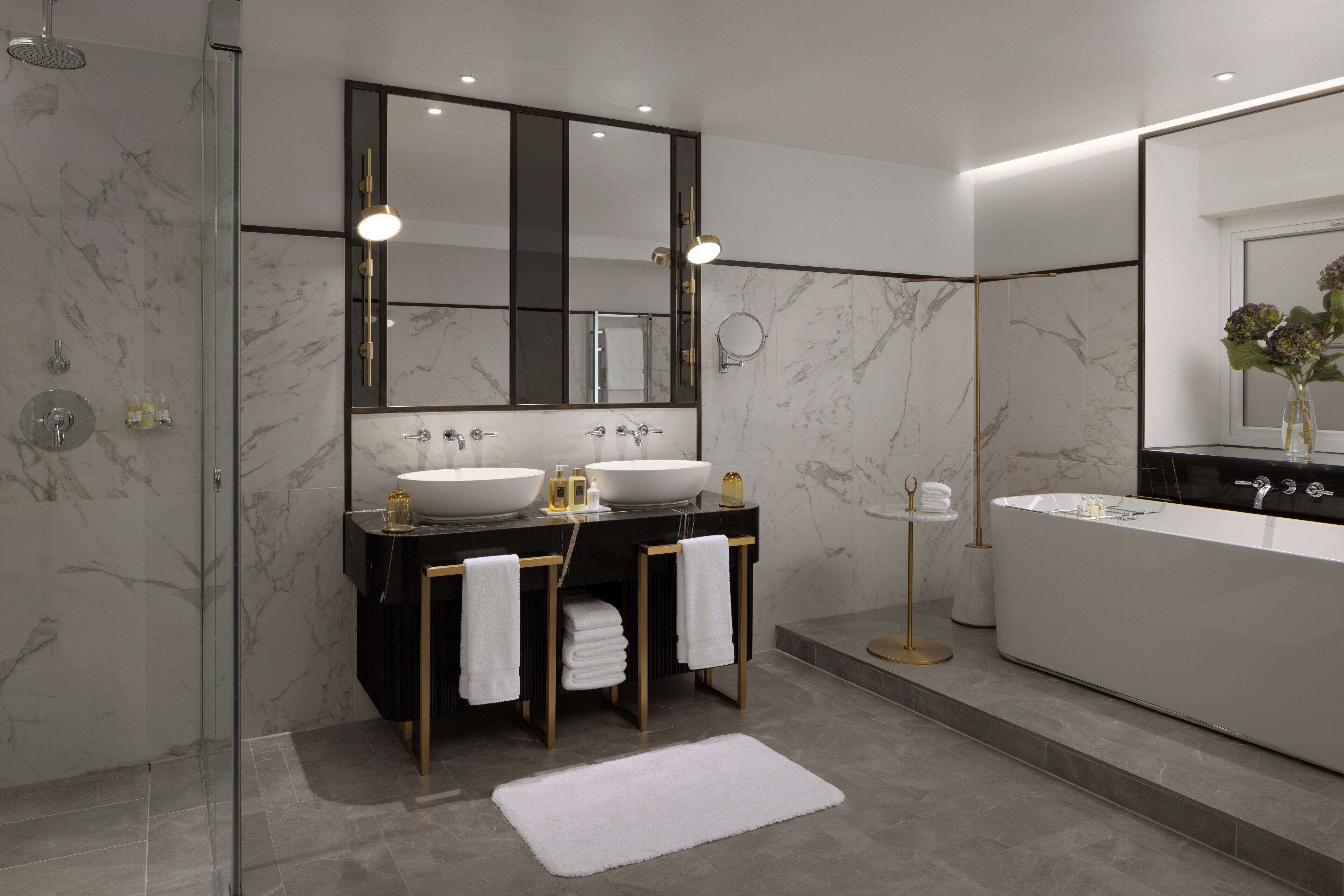 A modern bathroom with a glass-enclosed shower, two sinks with mirrors, a bathtub, and a white rug.