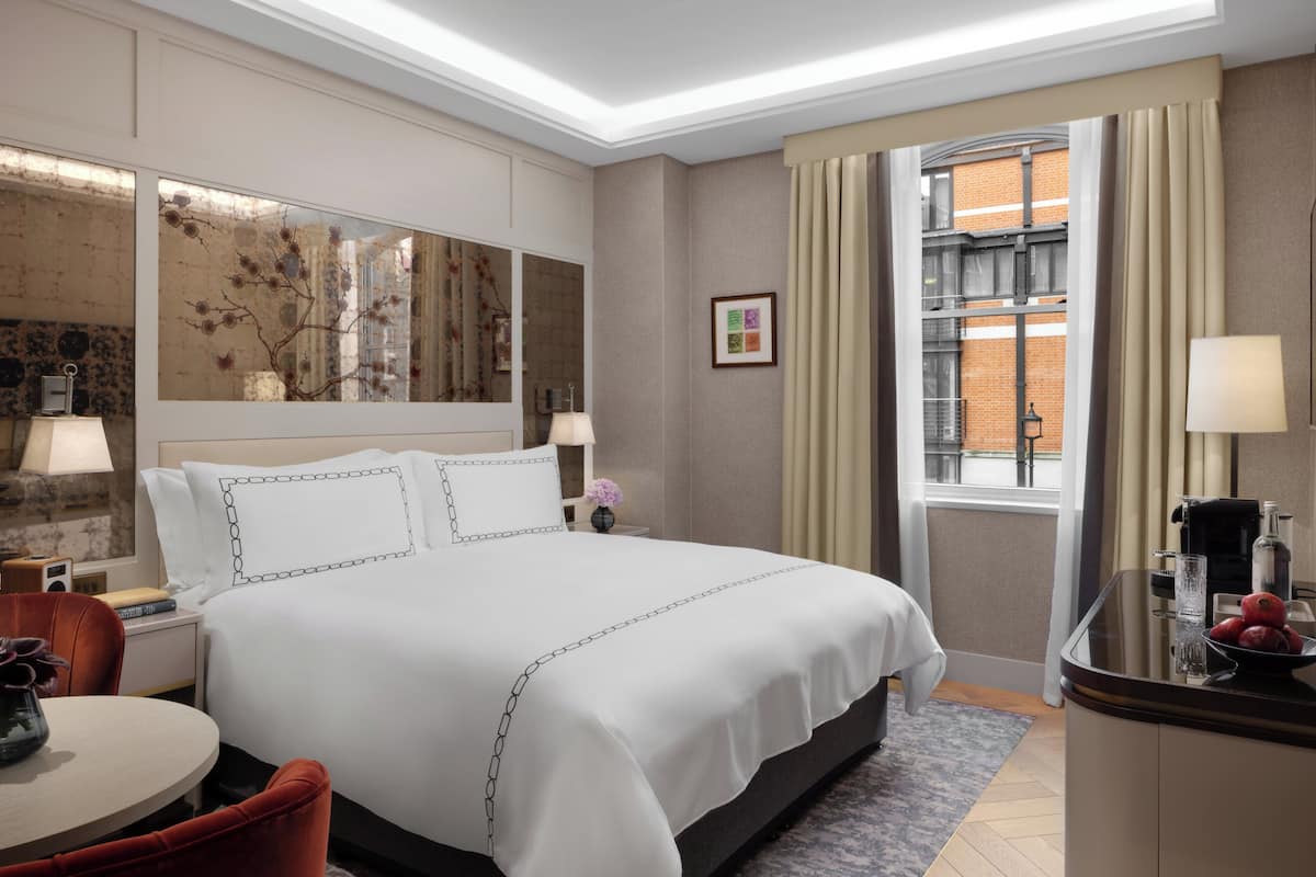 A hotel room with a large bed, bedside tables, a desk, and a window with curtains.