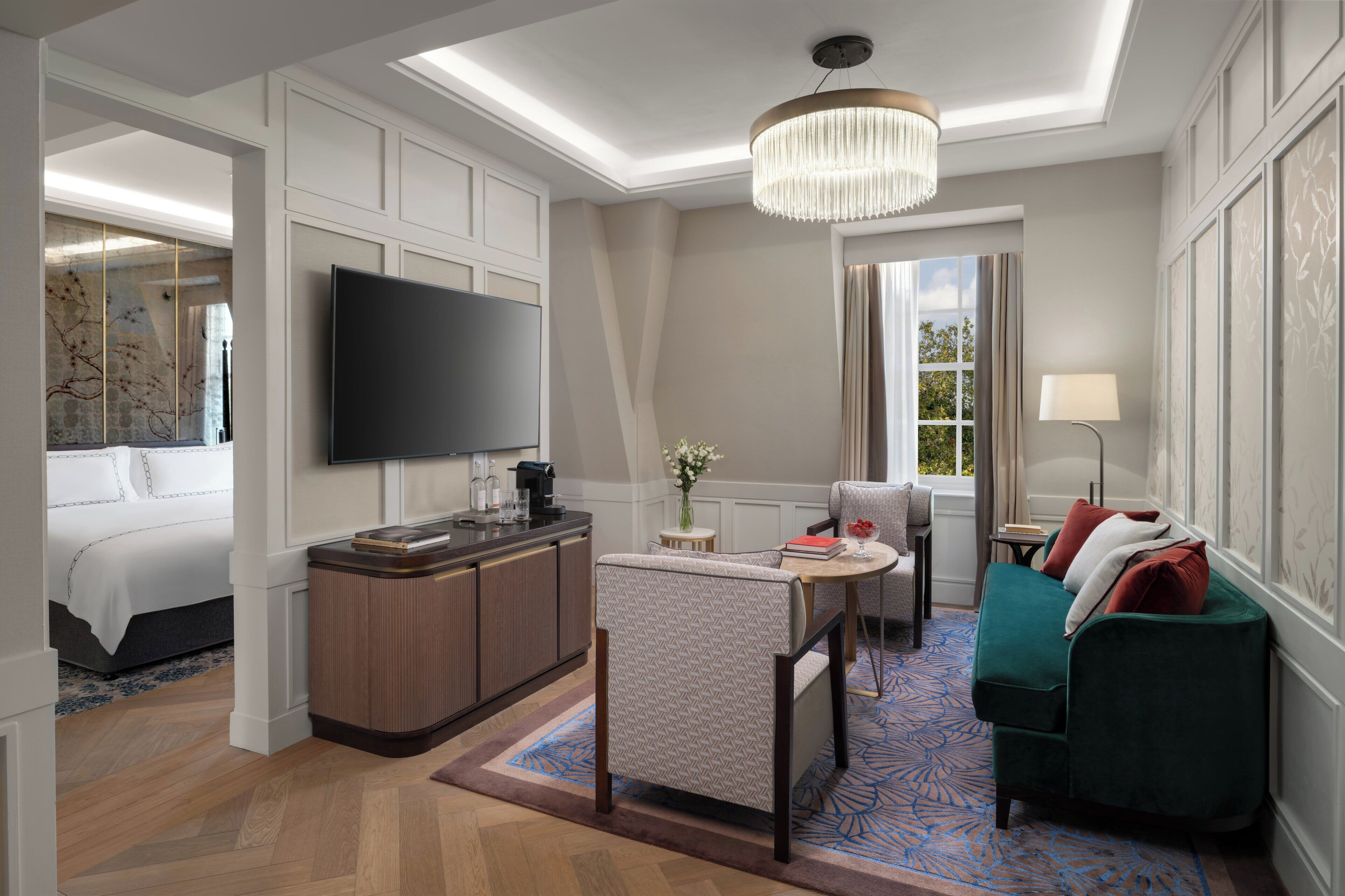 Een moderne hotelkamer met een flatscreen televisie, een groene bank, een kleine tafel met een vaas en een groot raam met gordijnen.