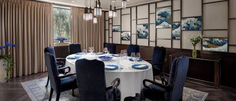 A dining room with a round table, blue upholstered chairs, and a white tablecloth.