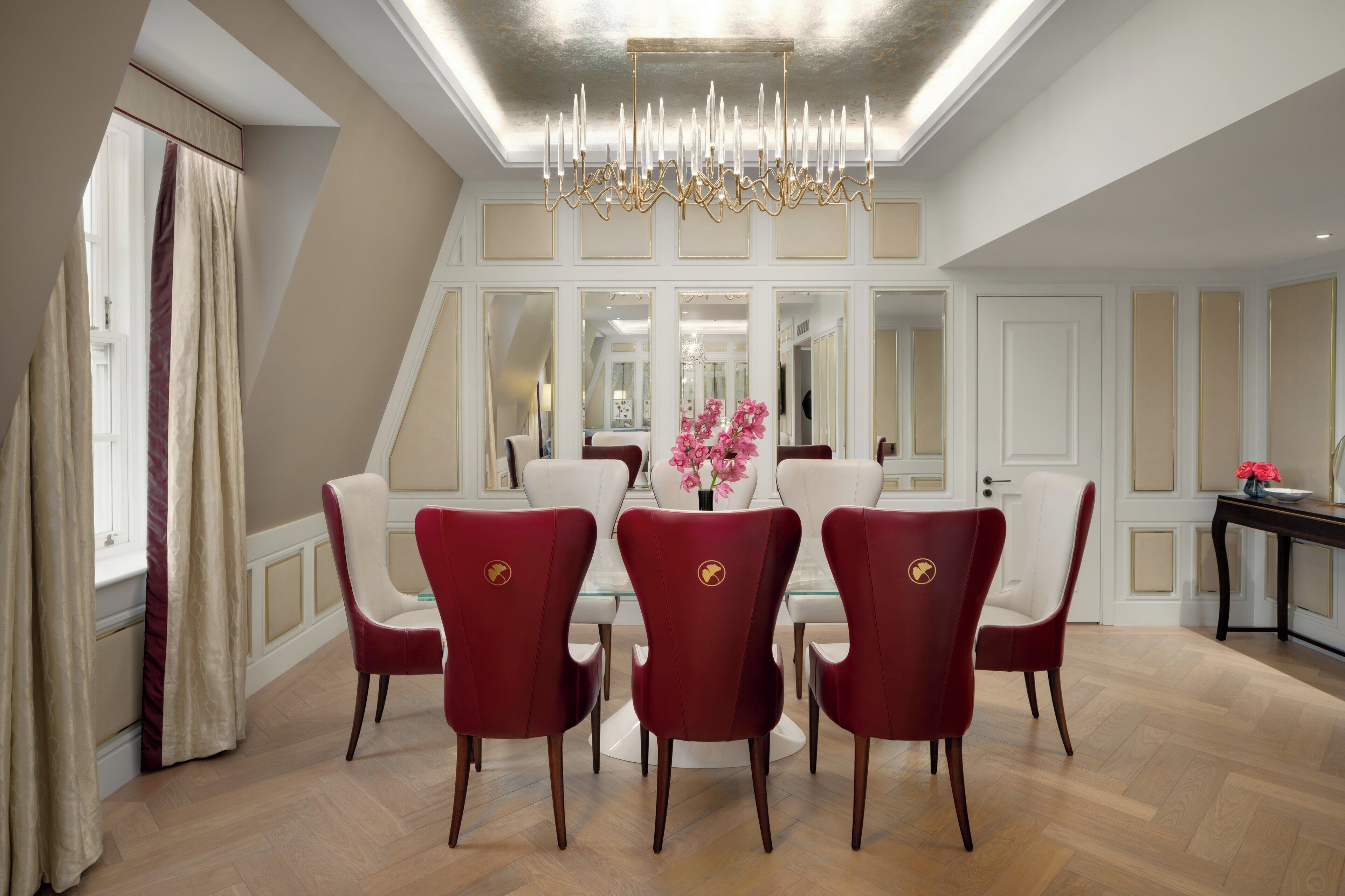 A dining area with a chandelier, red chairs, and a vase of flowers.