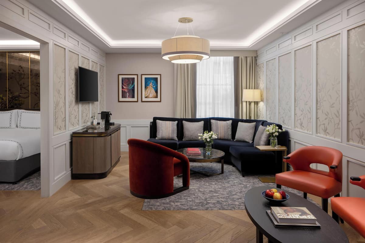 A modern living room with a sofa, red chairs, a coffee table, and a TV mounted on the wall.
