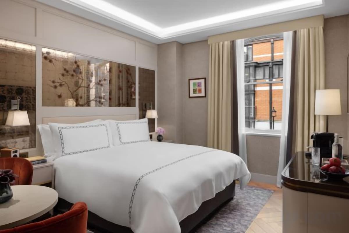 A hotel room with a large bed, a desk, a chair, a window with curtains, and a mirror on the wall.