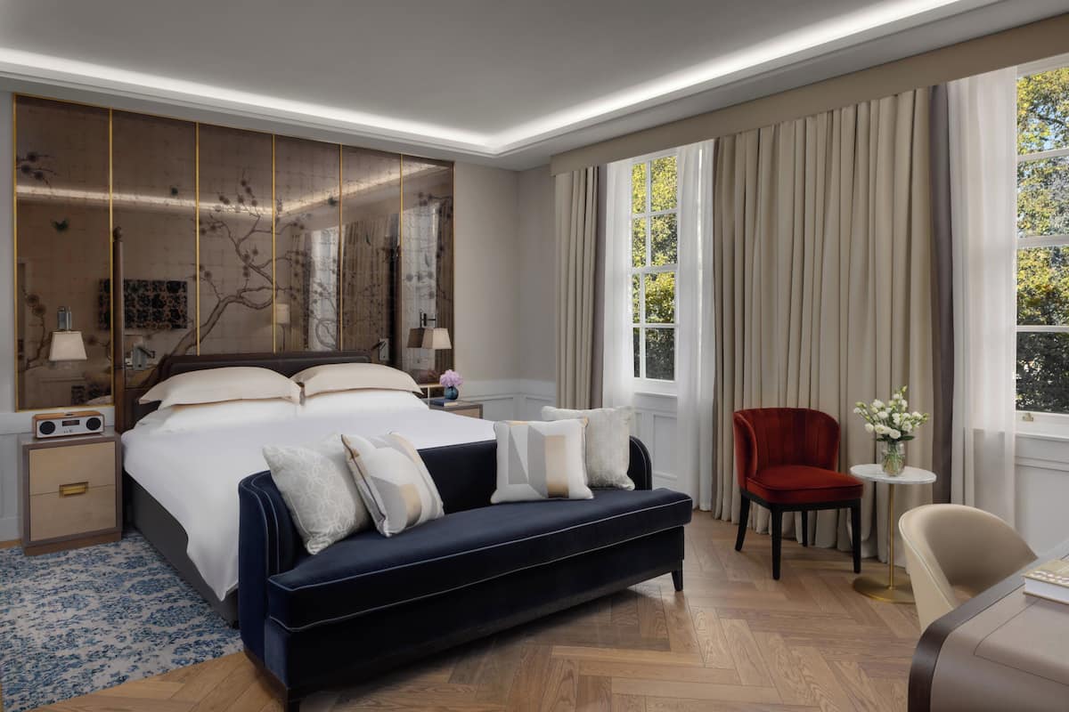 A modern hotel room with a large bed, a sofa, a chair, and a small table.