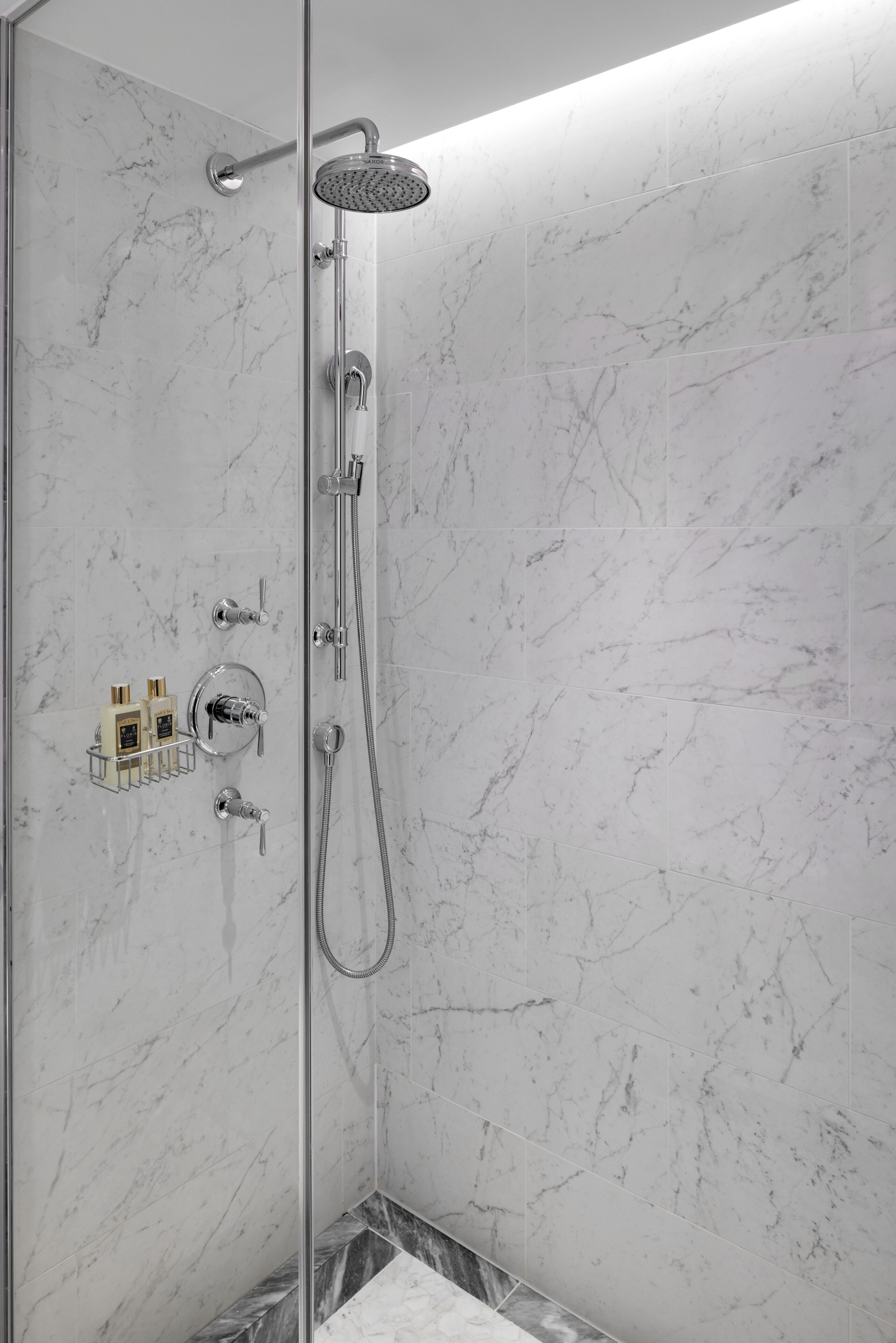 A modern shower with a glass door, chrome fixtures, and marble walls.