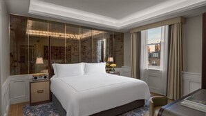 Un dormitorio amplio con una cama grande, una mesita de noche con radio, un espejo y vistas a la ciudad desde la ventana.