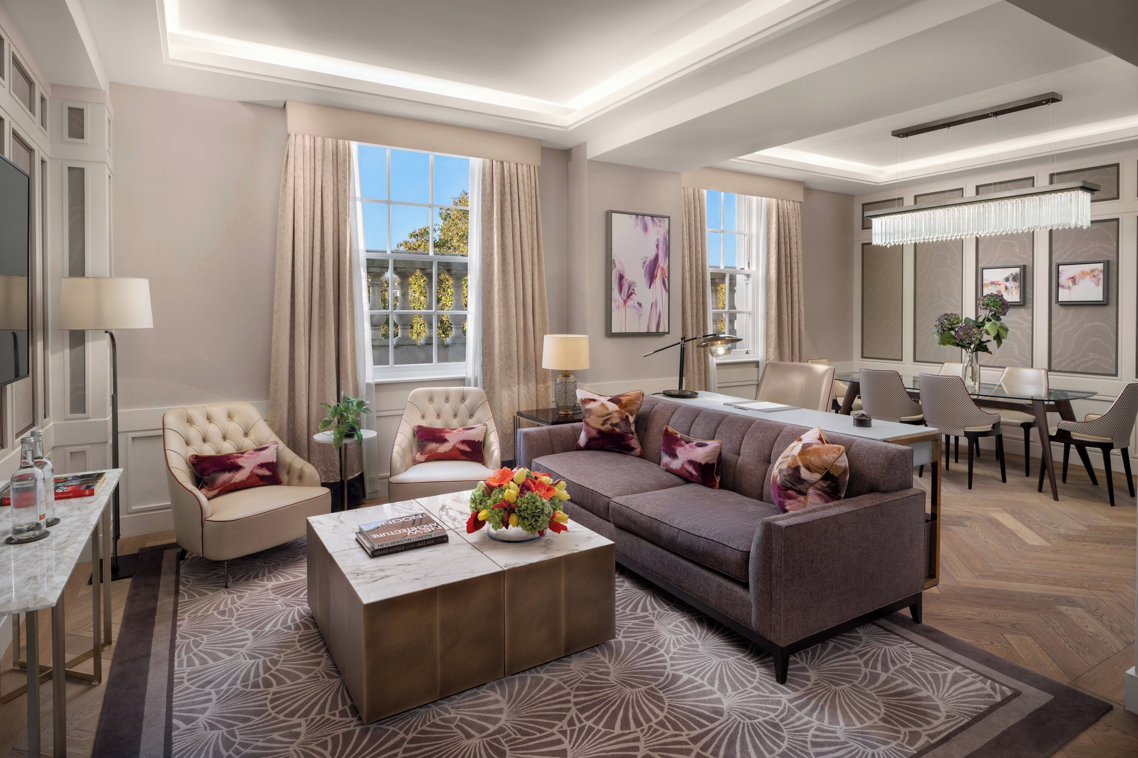 A modern living room with a sofa, armchairs, a coffee table, and a dining area with chairs and a table.